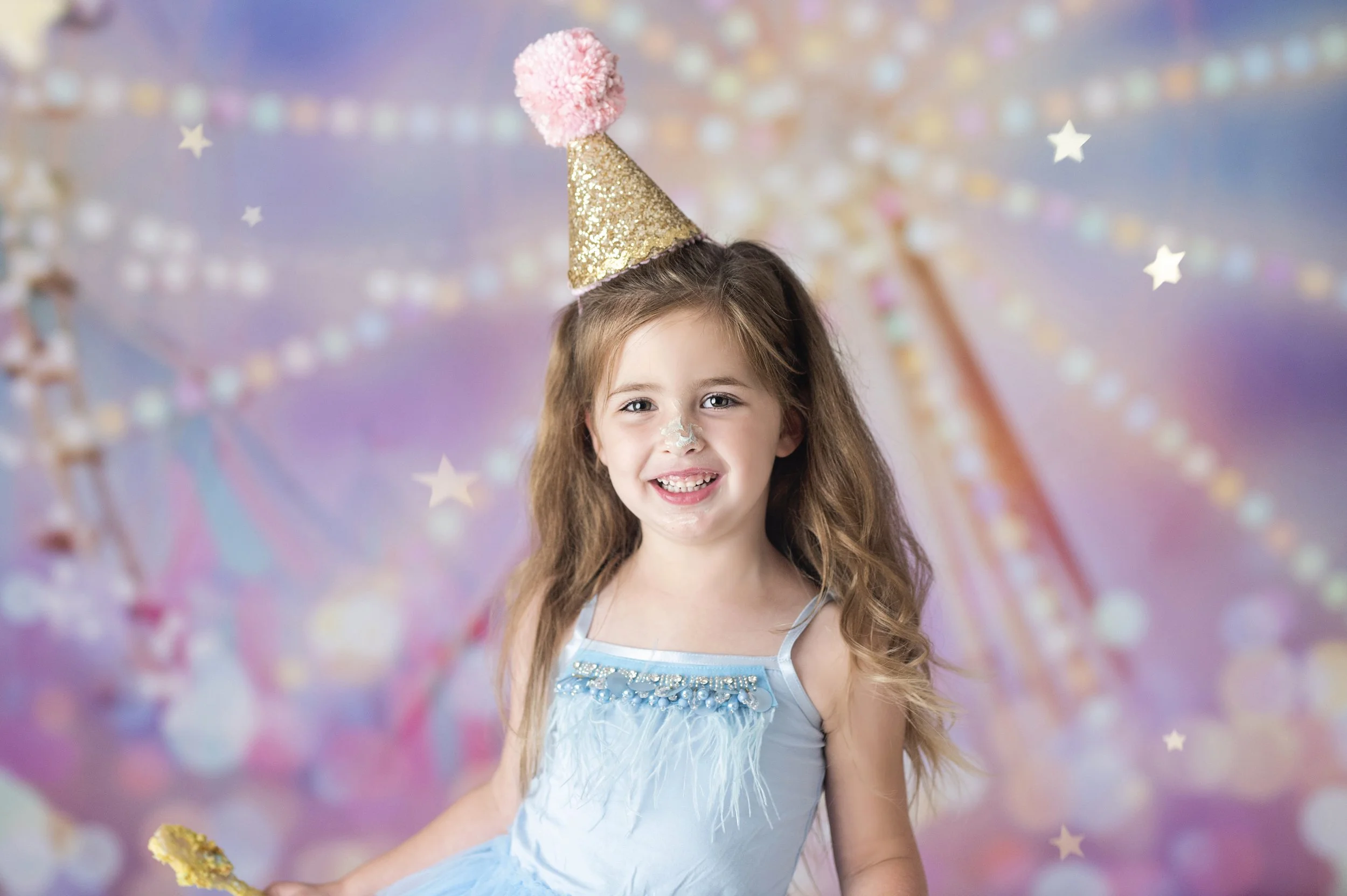 Young girl wearing a party hat during a colorful birthday milestone photography session.