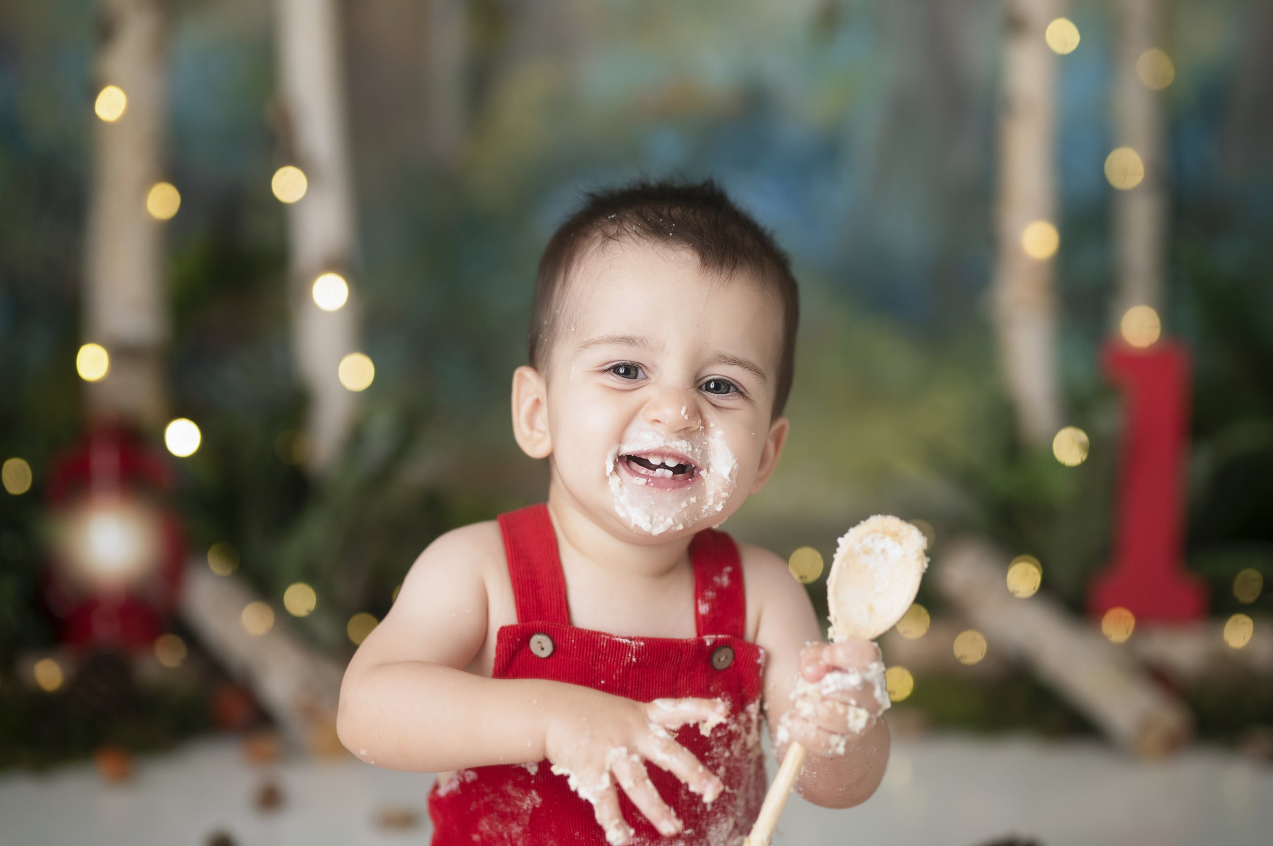 Smiling baby boy covered in frosting during a first birthday Cake Smash photography session.