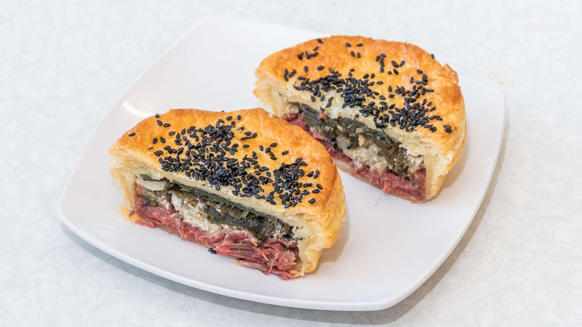 Sliced palusami pie filled with corned beef and taro leaves, topped with black sesame seeds, on a white plate.