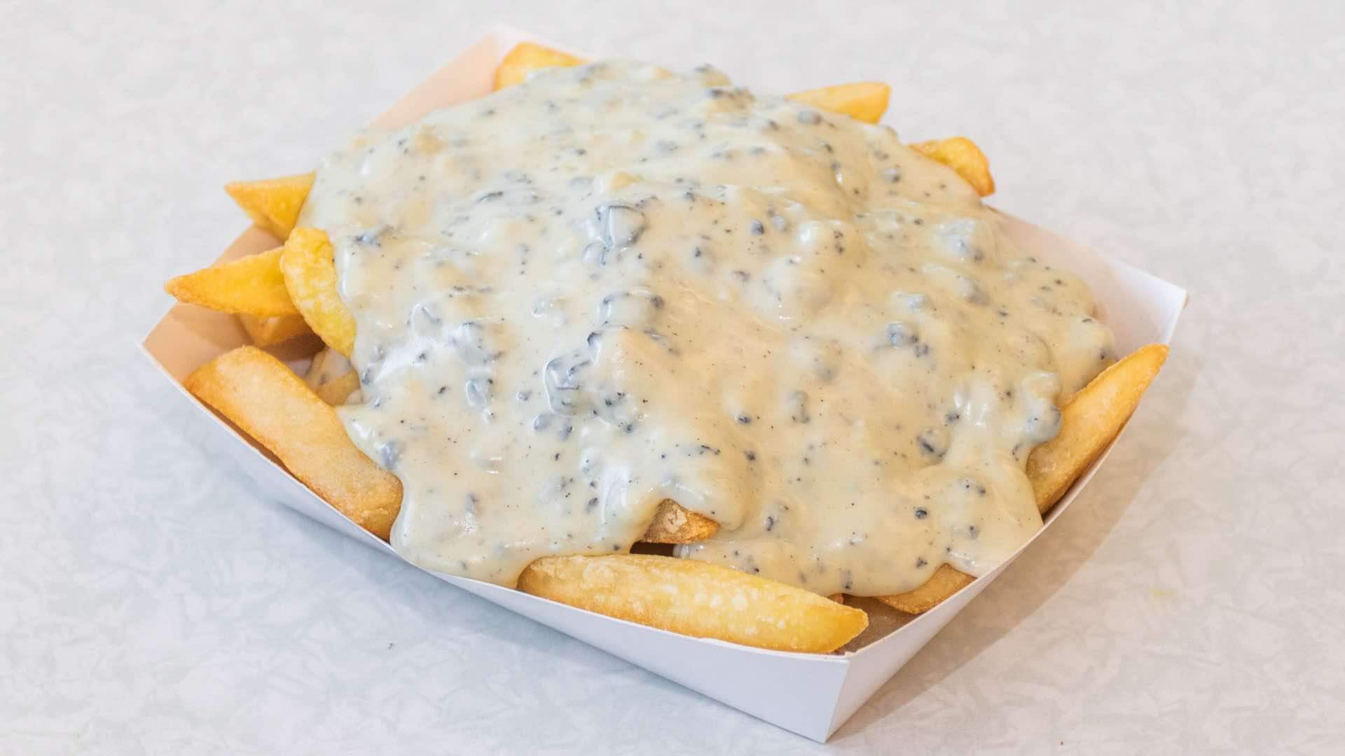 Fries topped with creamy paua sauce, served in a white paper tray.