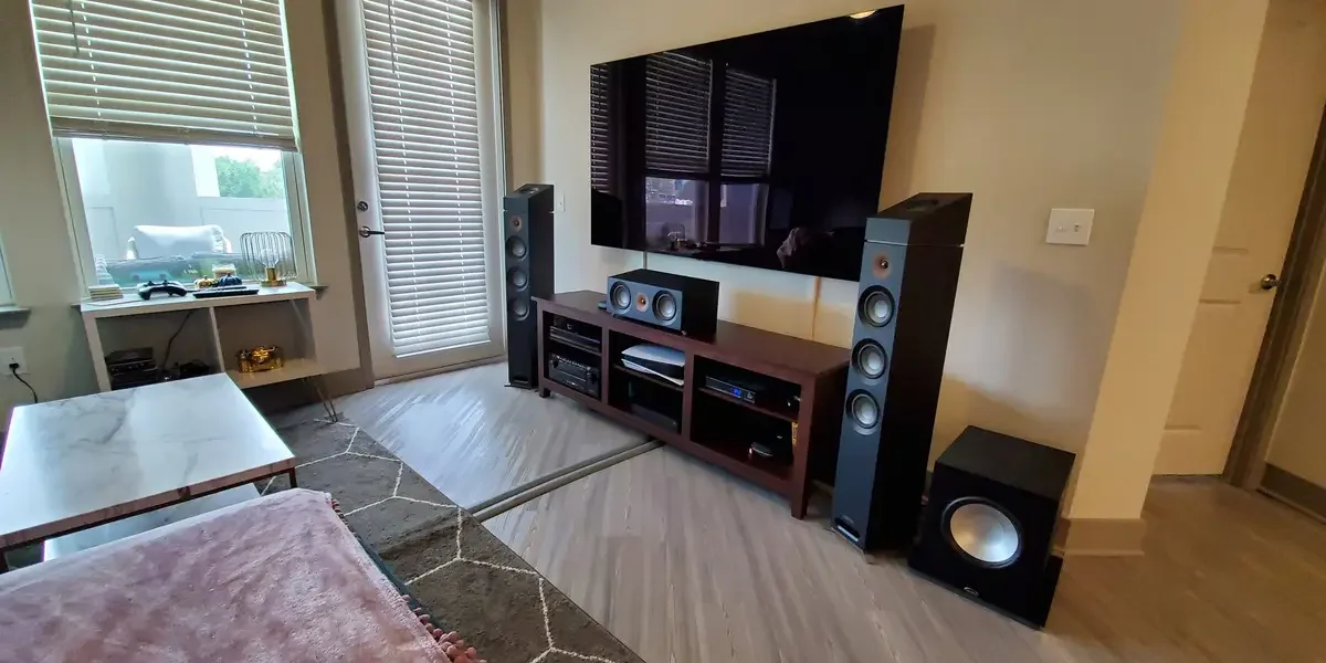 Wall-mounted TV and surround sound system with floorstanding speakers, center channel, and subwoofer in a finished living room.