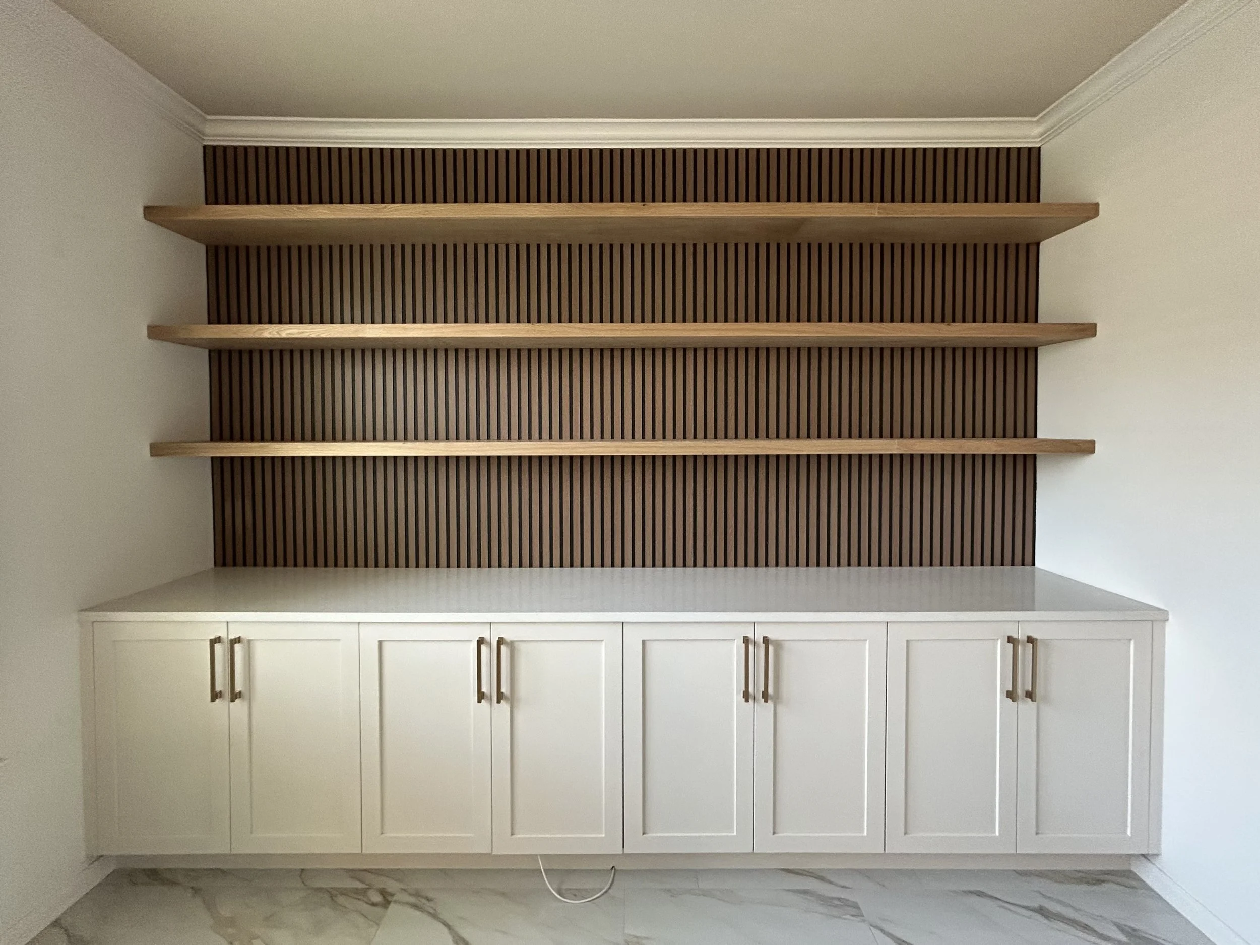 This client in San Antonio wanted to add storage and shelving to their empty wall. We were able to to add a wall of built in cabinets with stunning quartz countertops to this homes office area. The slat wall behind the floating shelves gave it really