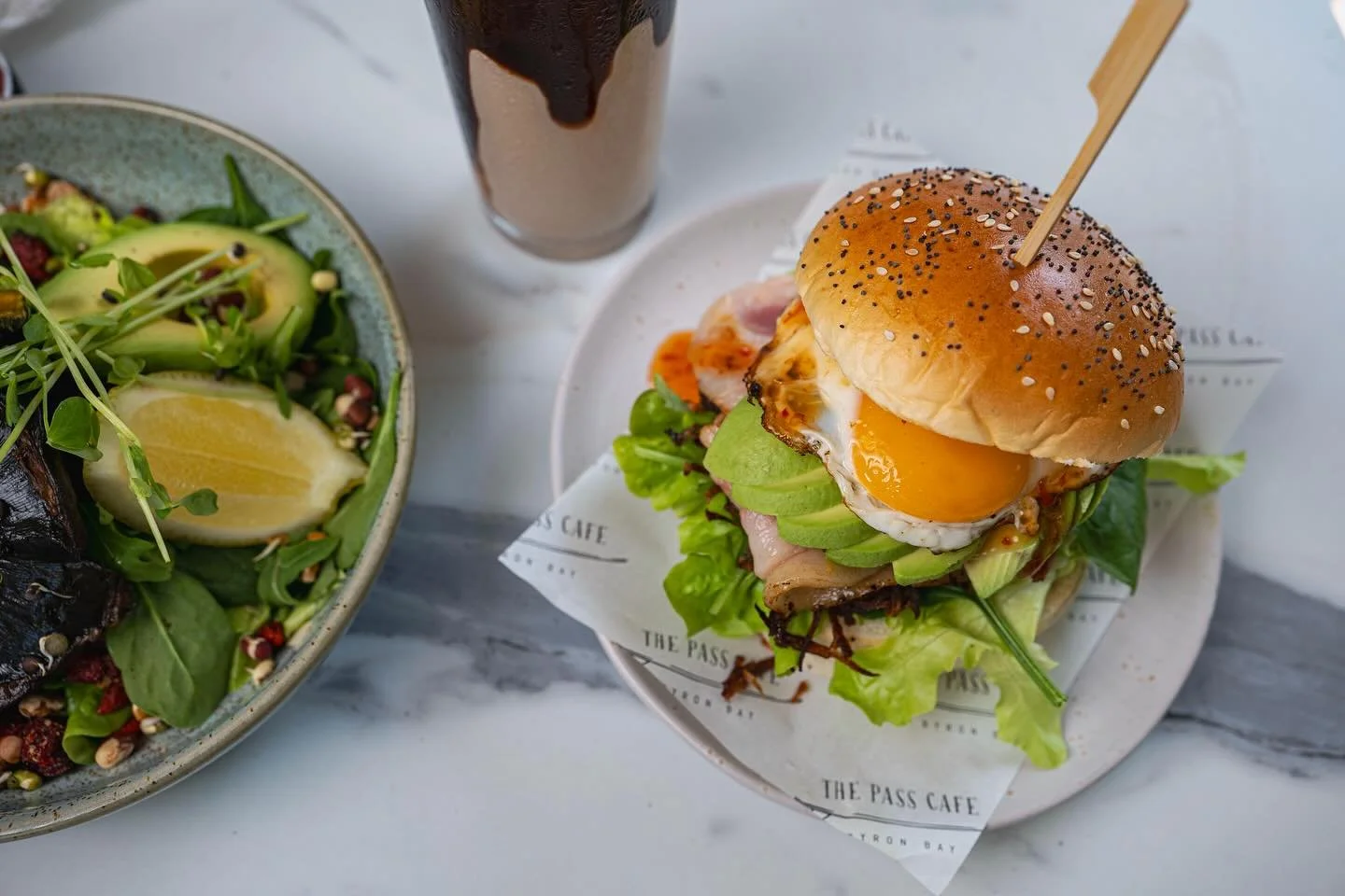 🌈💕🌴 The Pass Cafe&rsquo;s iconic Brekky burger 🌴💕🌈. Avocado, crispy hash, runny egg, and a whole lotta flavour &mdash; this is how we do mornings at The Pass Caf&eacute; 🩵