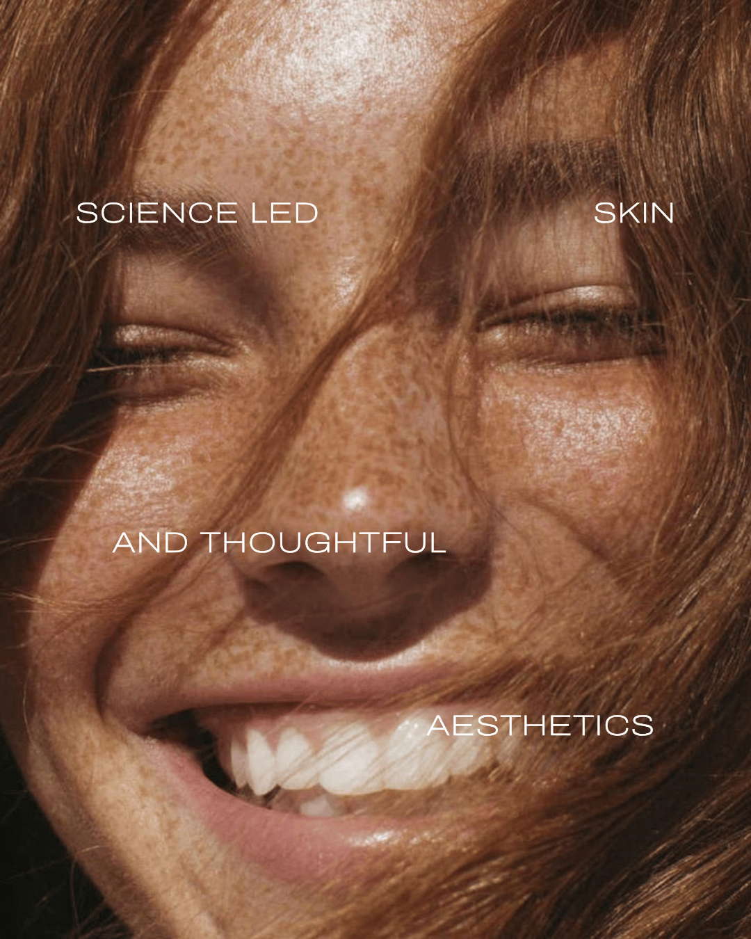 Close-up of a woman's smiling face with red hair, showing words overlayed: 'SCIENCE LED,' 'SKIN,' 'AND THOUGHTFUL,' and 'AESTHETICS'.