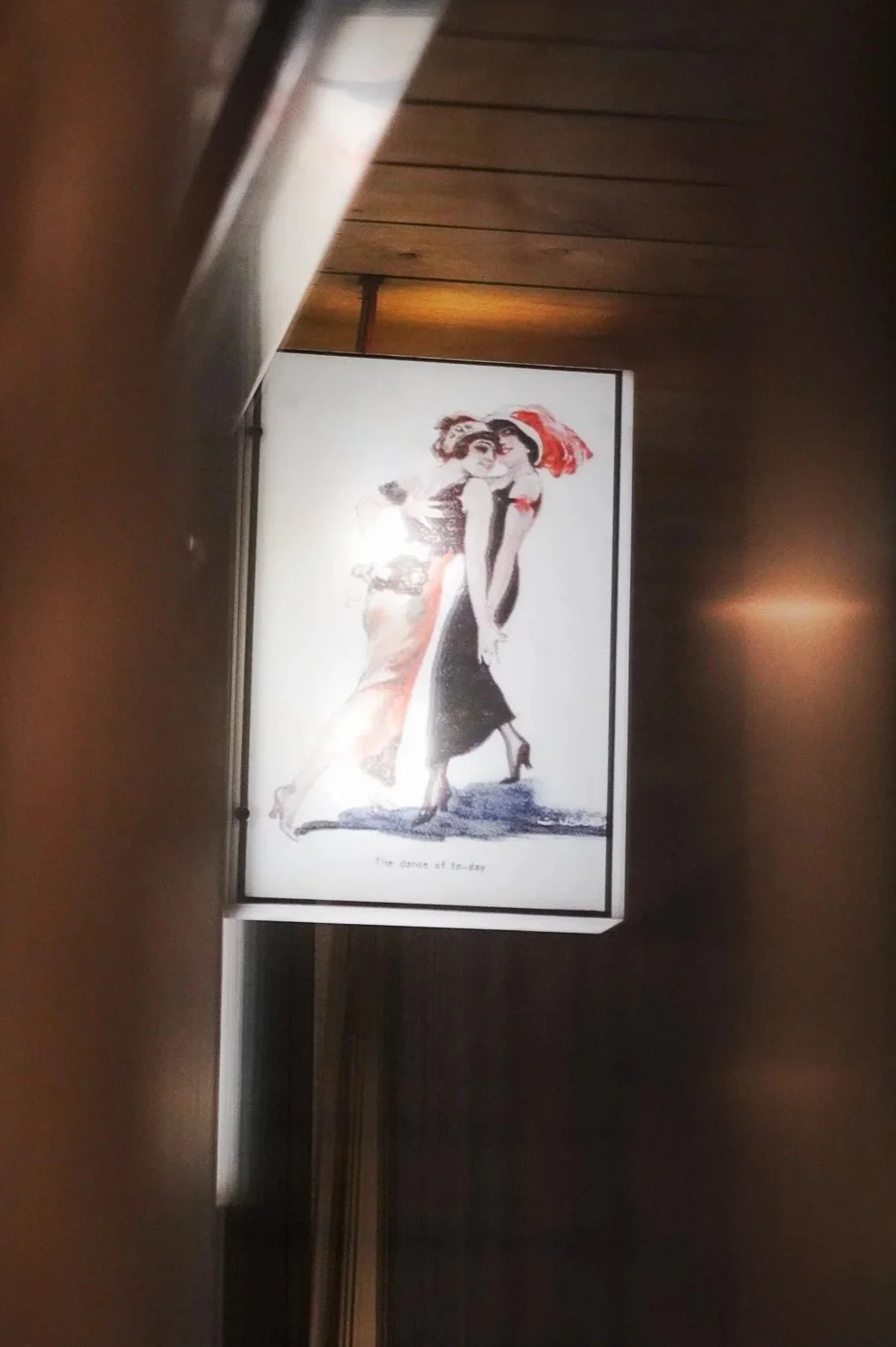 A framed poster of two women dancing, dressed in vintage clothing, with the caption "The dance of to-day".