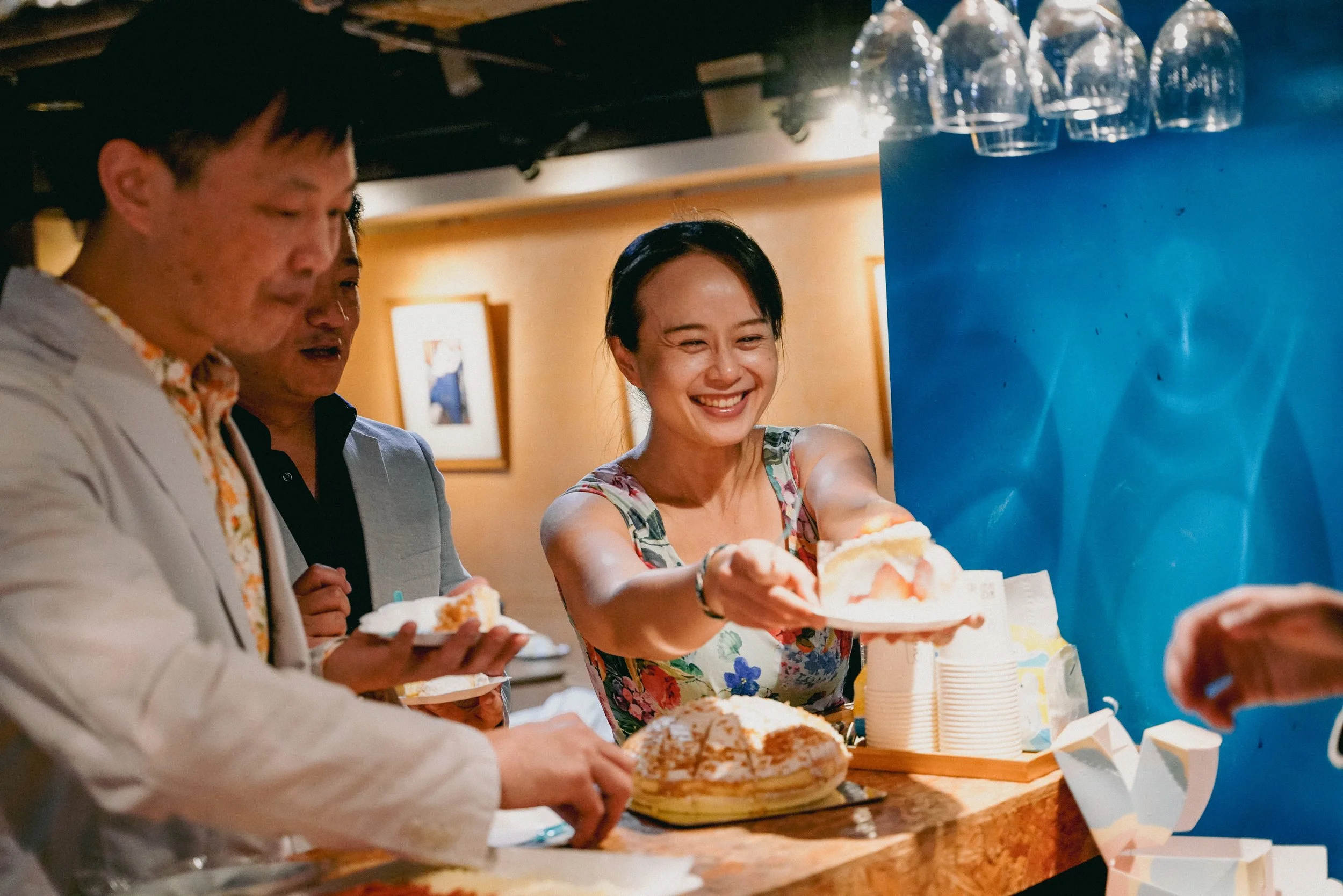 People at a celebration serving and enjoying slices of cake and drinks.
