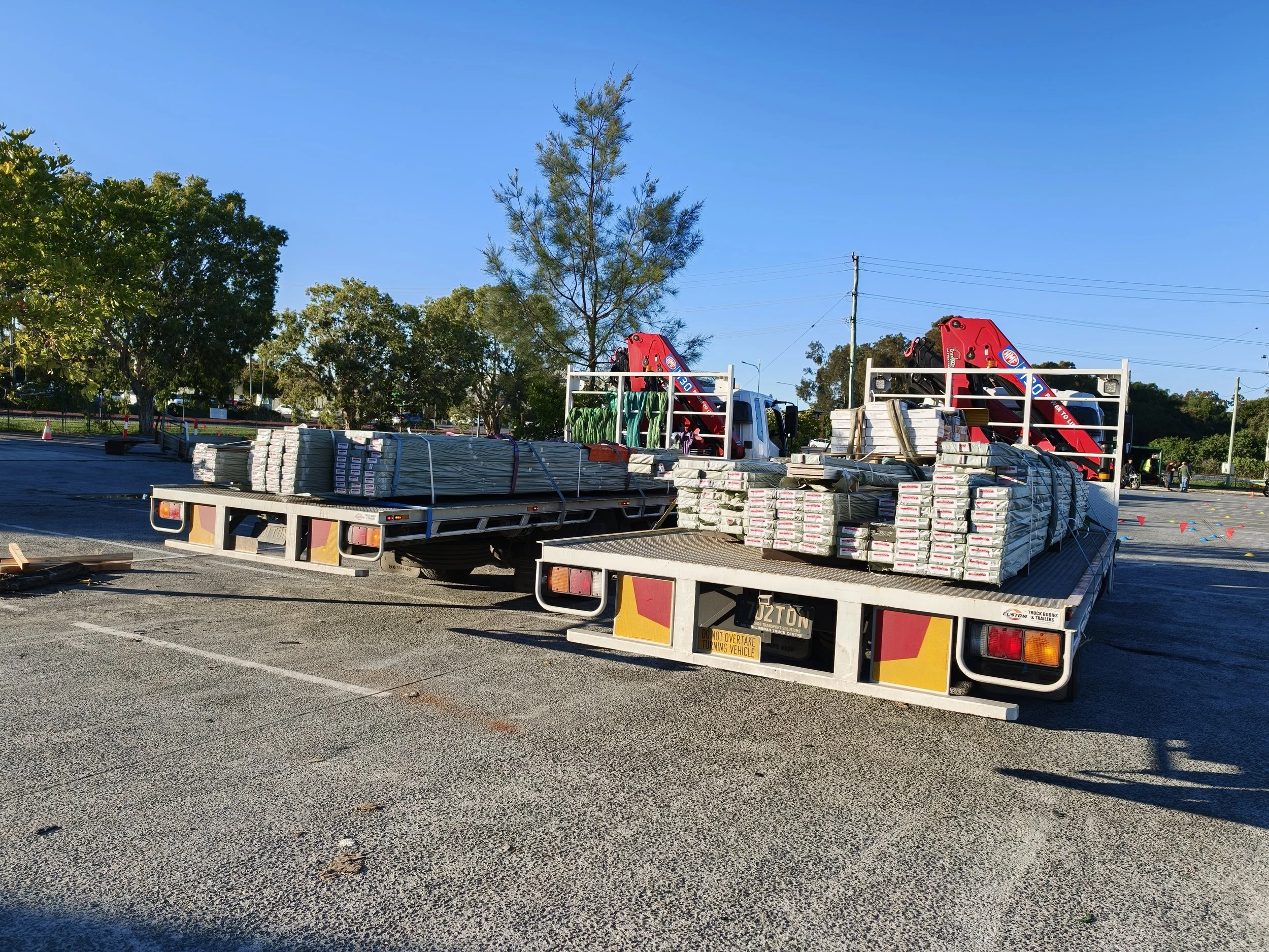 Two crane trucks parked in a car park, loaded with building materials.