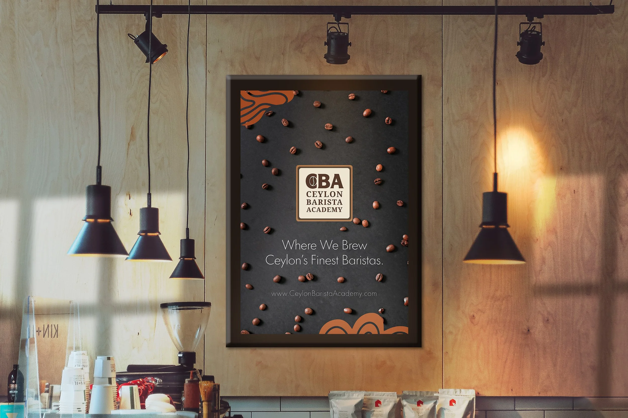 Sign for Ceylon Barista Academy with coffee beans and patterns, framed on the wall in a coffee shop, surrounded by hanging pendant lights.