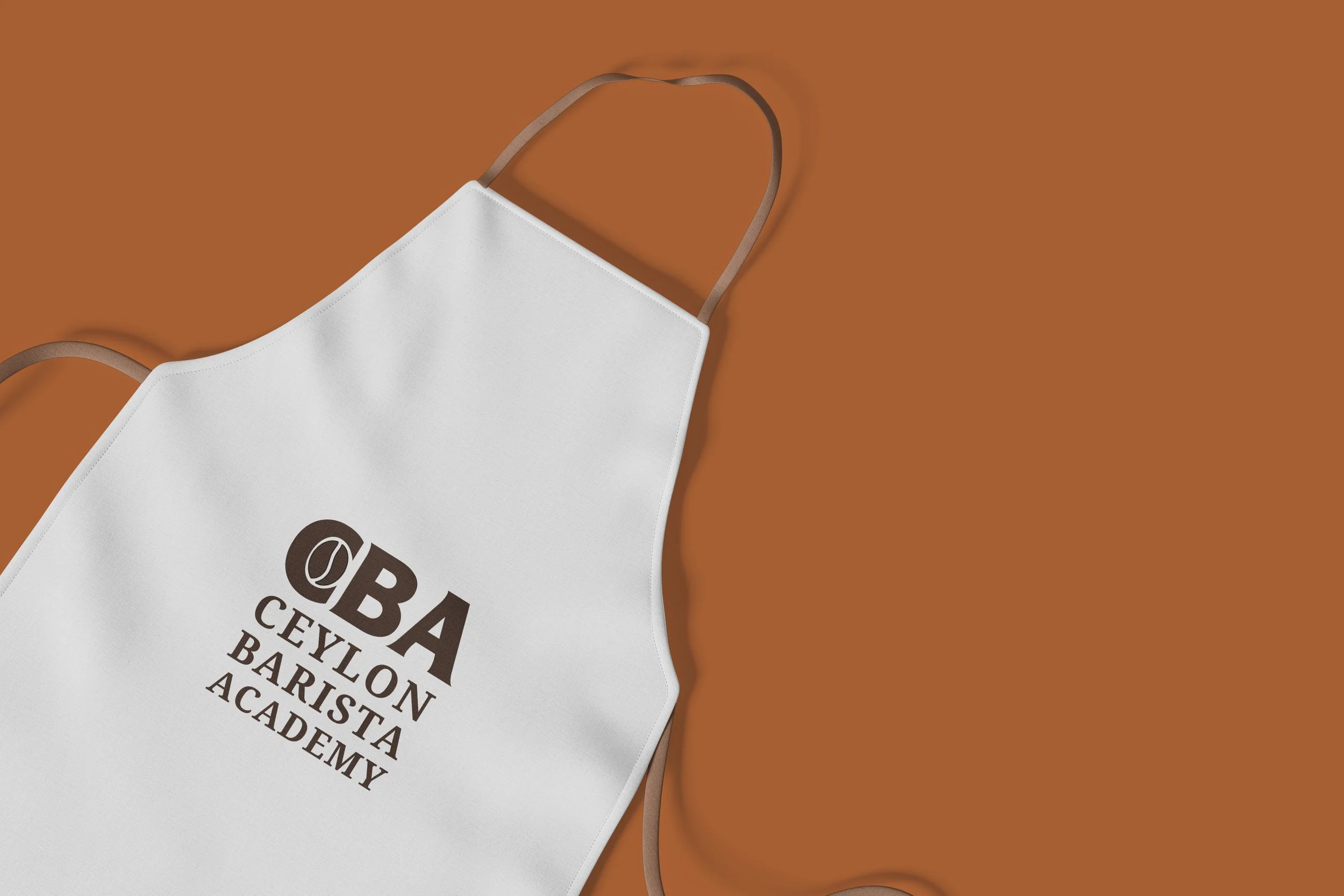Close-up of a white face mask with brown elastic straps on a brown background, with part of the text visible that reads 'CBA CEYLON BARI...'