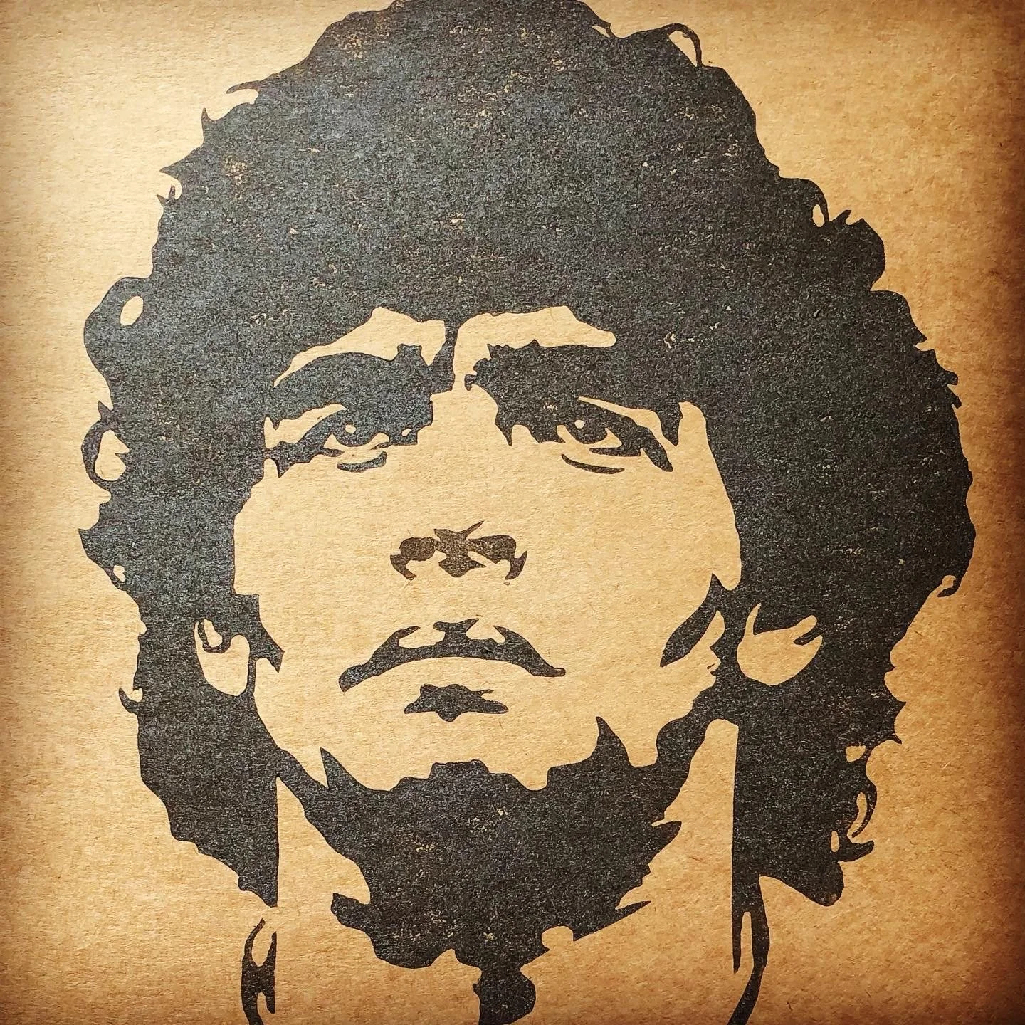 Stencil art of a person with glasses and long hair, with a serious expression, painted on a wooden surface.