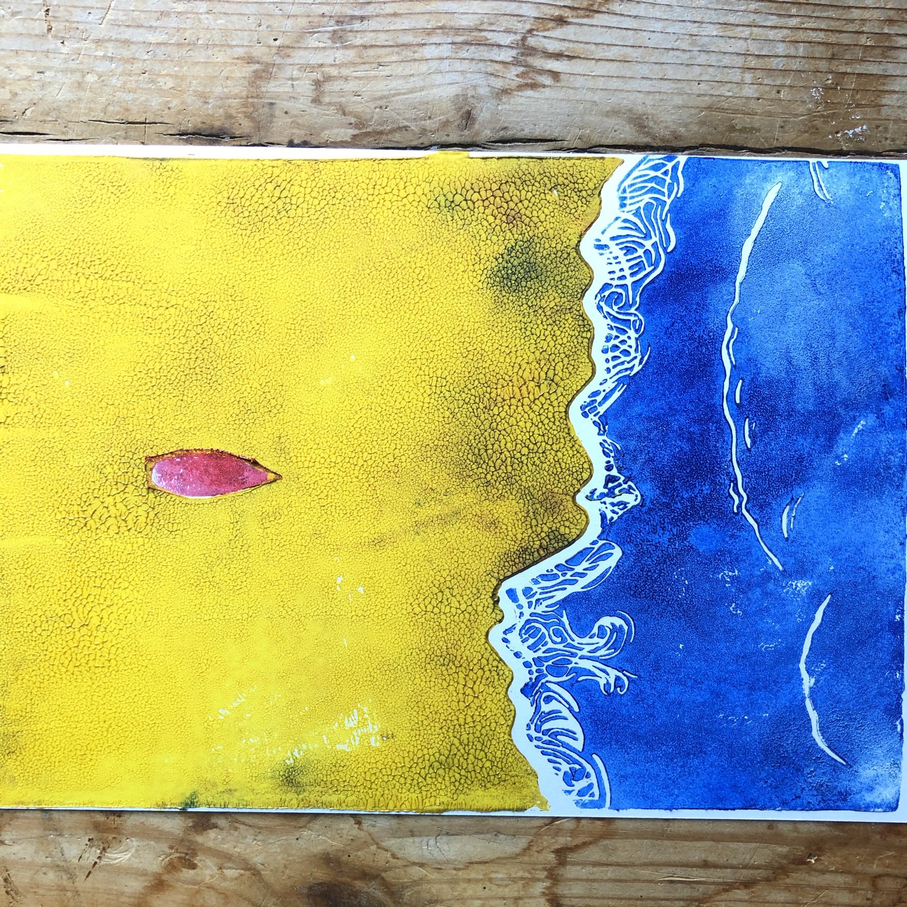 A colorful abstract painting with yellow, blue, pink, and black hues. The painting is on a flat surface, with a wooden background underneath.