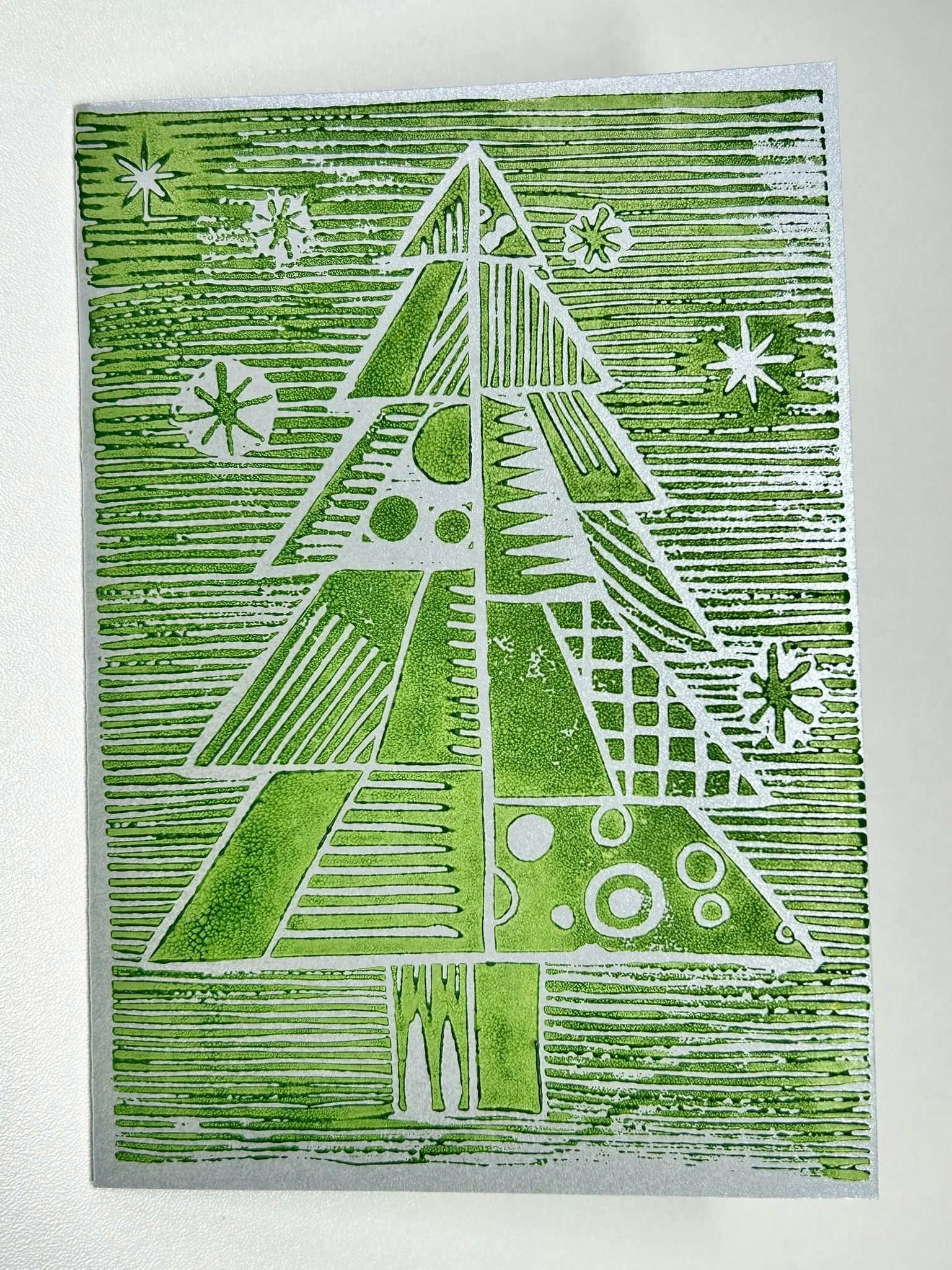 Green metallic stencil art of a stylized Christmas tree with snowflakes around it.