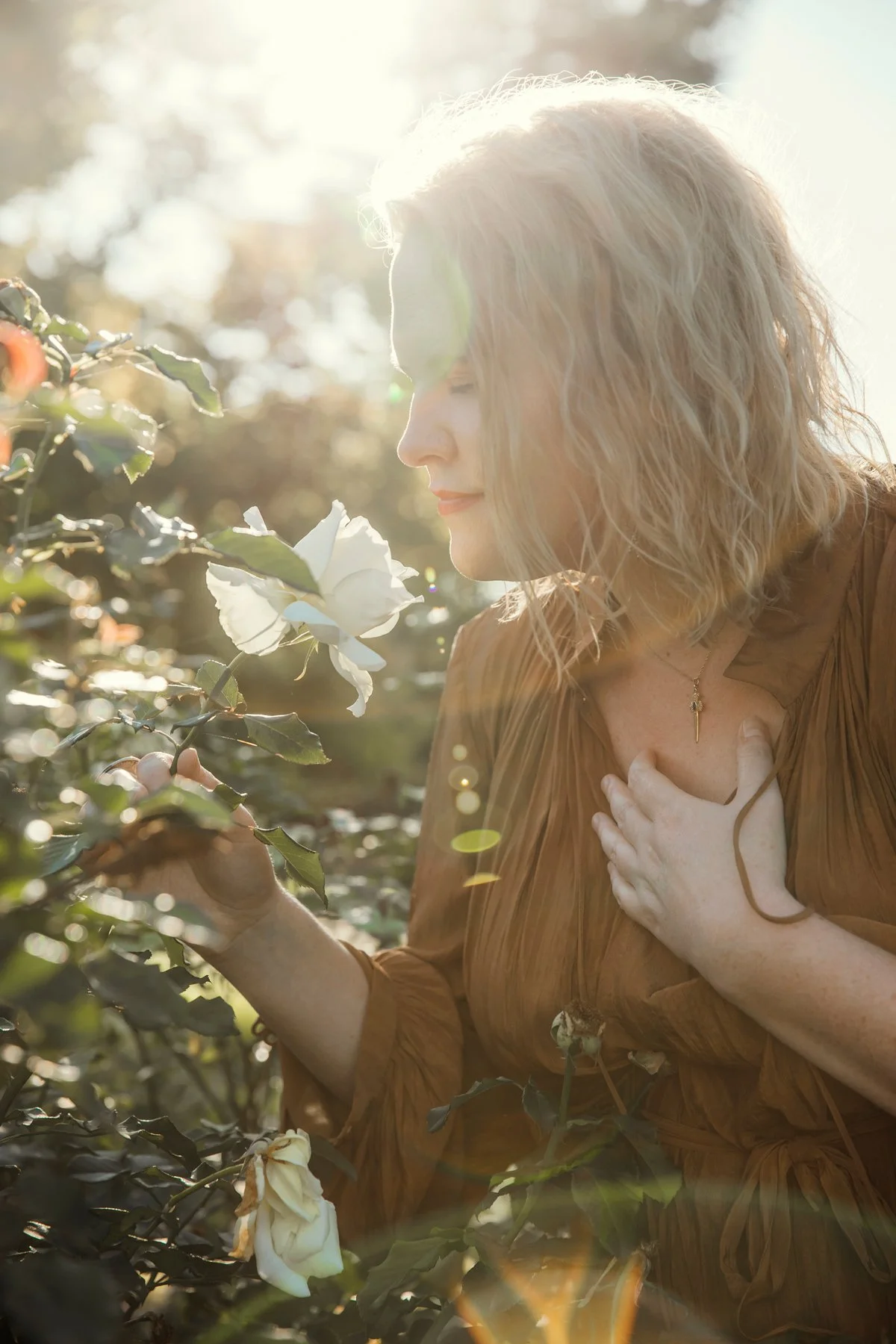 Brisbane outdoor portrait of a woman with curly blonde hair touching white flowers, backlit by golden sunlight, by Lisa Ray Photography