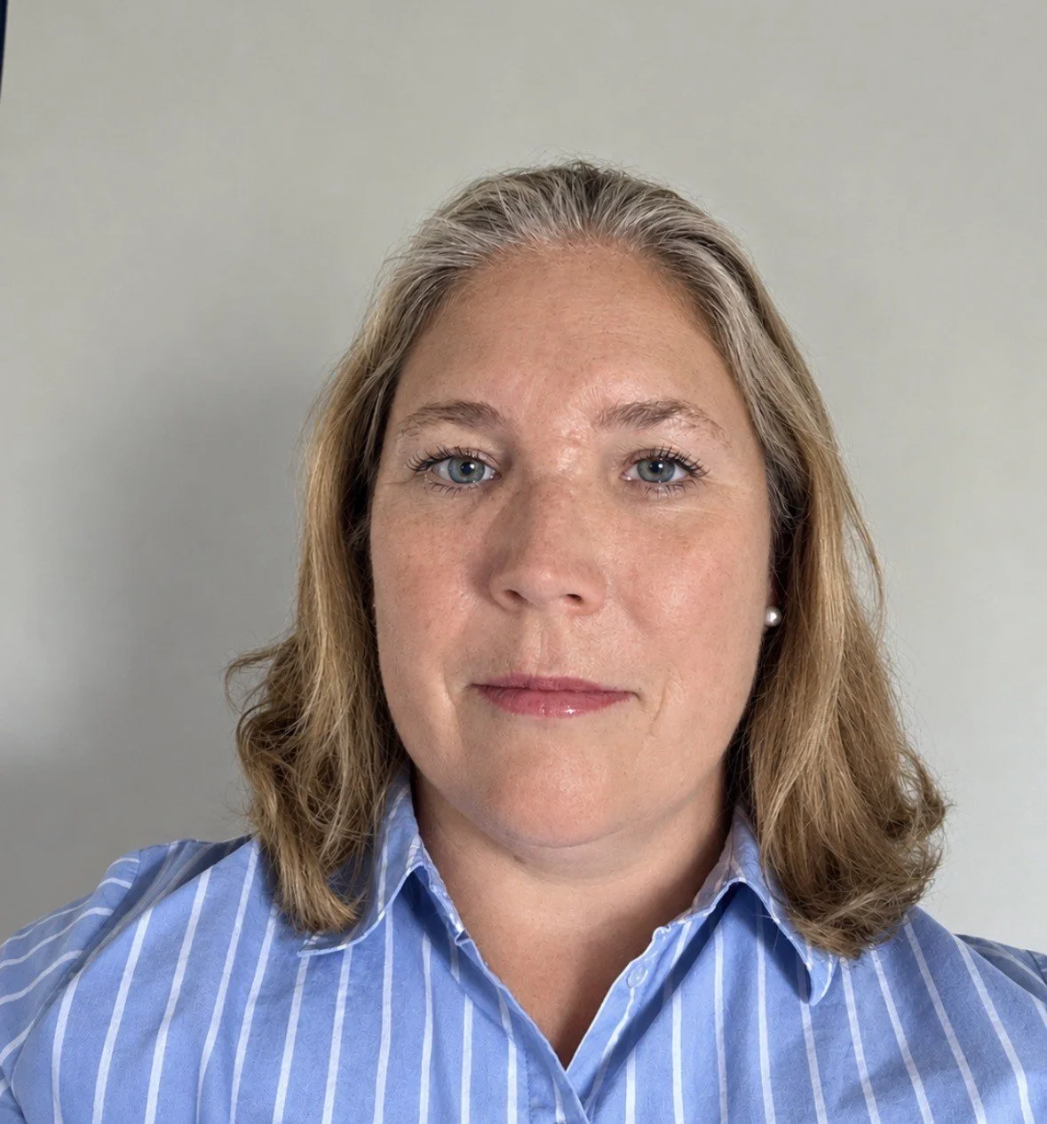 Close-up portrait of a woman with blonde hair, blue eyes, wearing a blue and white striped shirt and pearl earrings, against a plain background. Planning Consultant