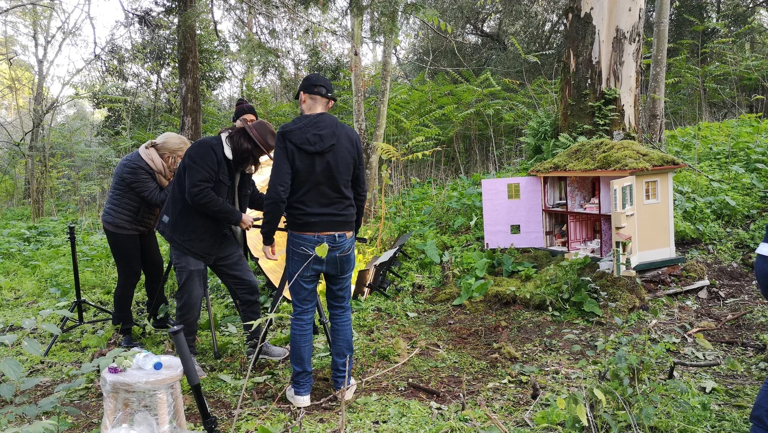 Group of people filming or photographing a dollhouse in a forest.