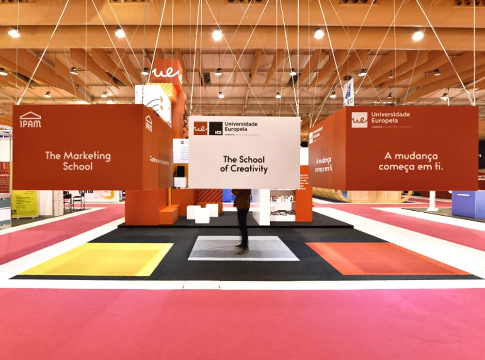 Exhibition booth for Universidade Europeia with signs displaying 'The Marketing School', 'The School of Creativity', and 'A mudança começa em ti'.
