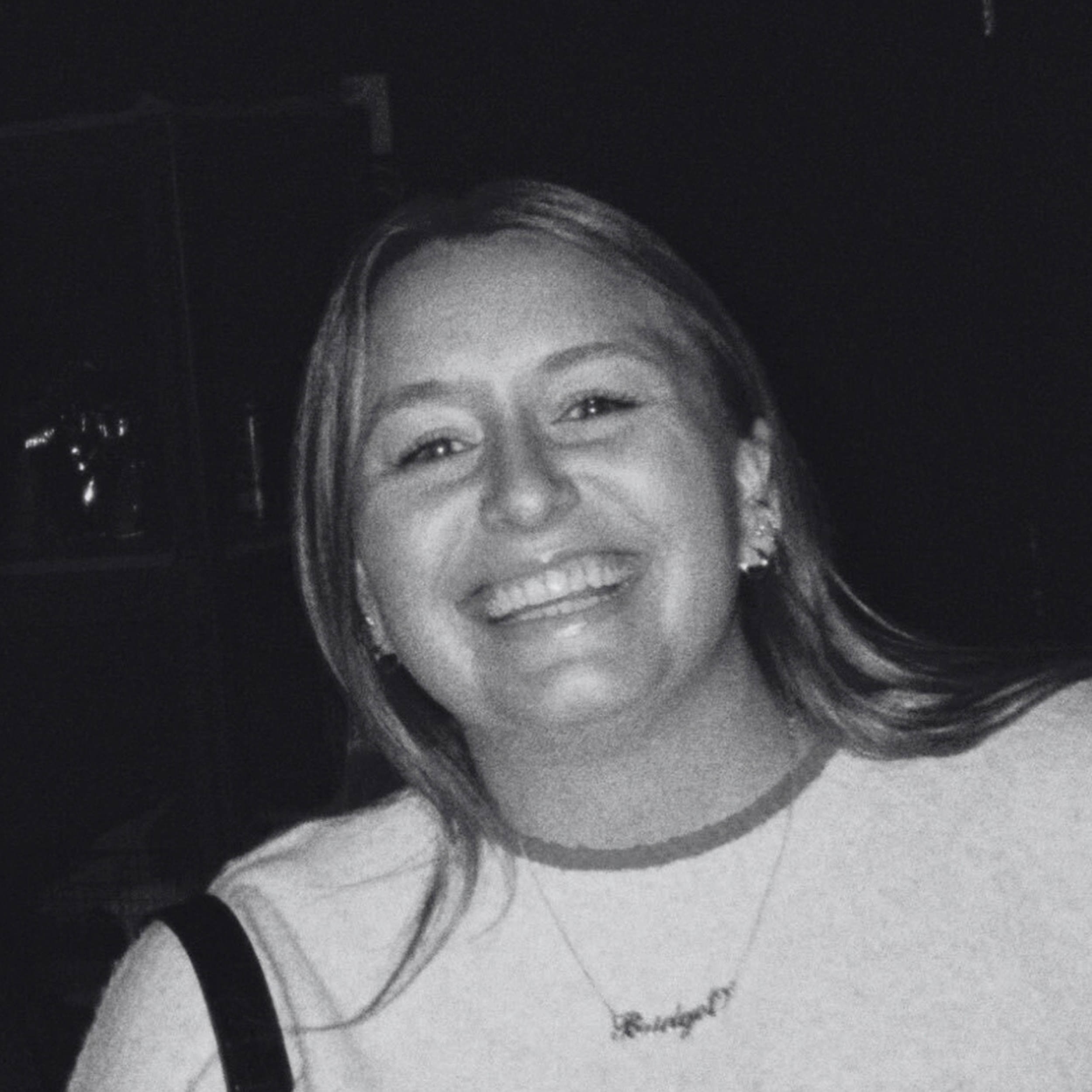 Black-and-white close-up portrait of a smiling woman with long hair and earrings.