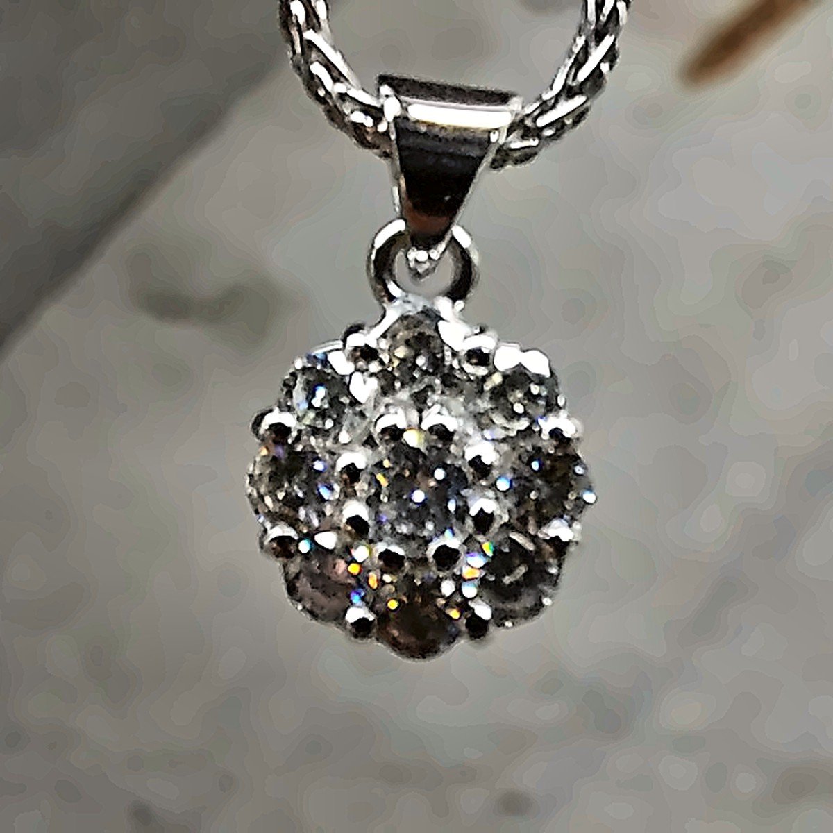 A white gold necklace with a pendant made of small sparkling black and clear gemstones, hanging from a chain.