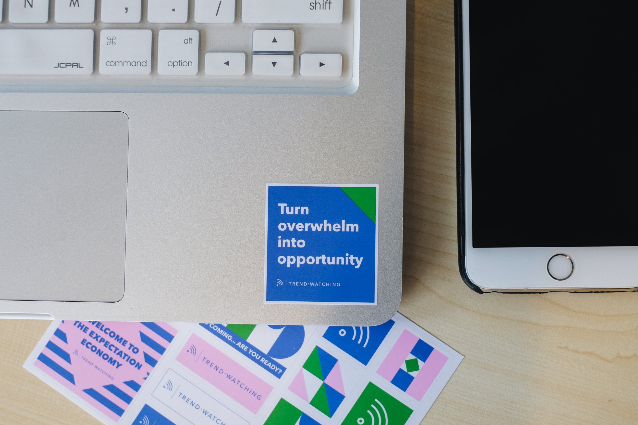 Trend Watching "Turn overwhelm into opportunity" square vinyl laptop sticker beside a geometric blue, pink and green sticker sheet – conference sticker merchandise, retail merchandise Malaysia