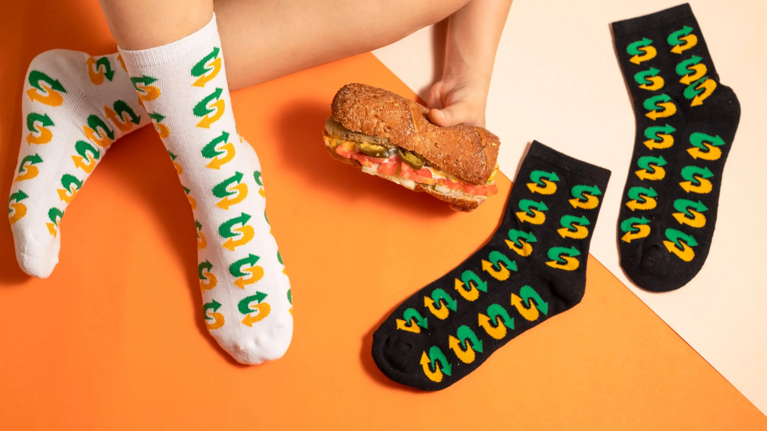 Custom logo socks for a food brand Subway in white and black, worn and laid flat beside a sandwich