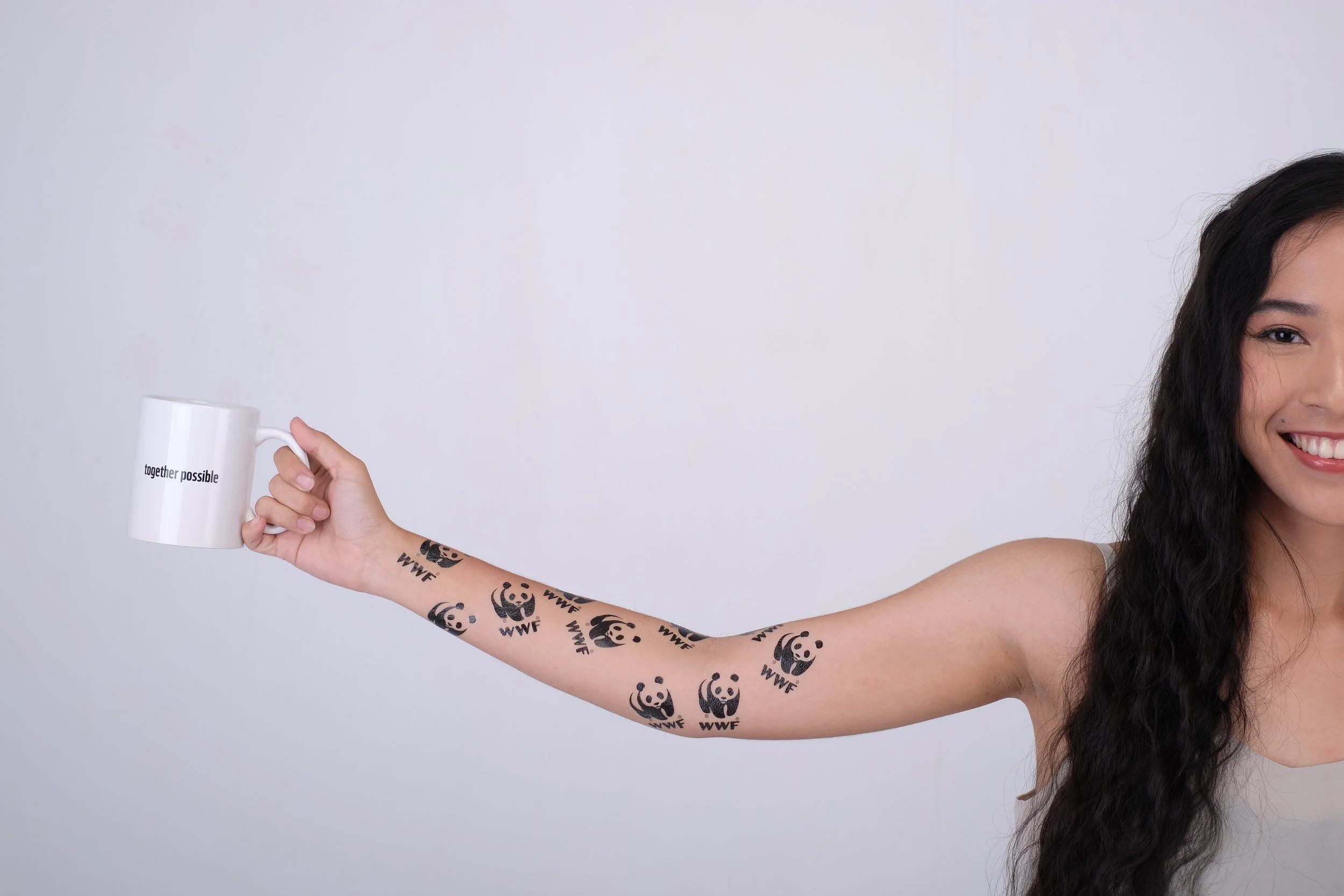Row of WWF panda logo temporary tattoos along an arm, holding a Together Possible branded mug