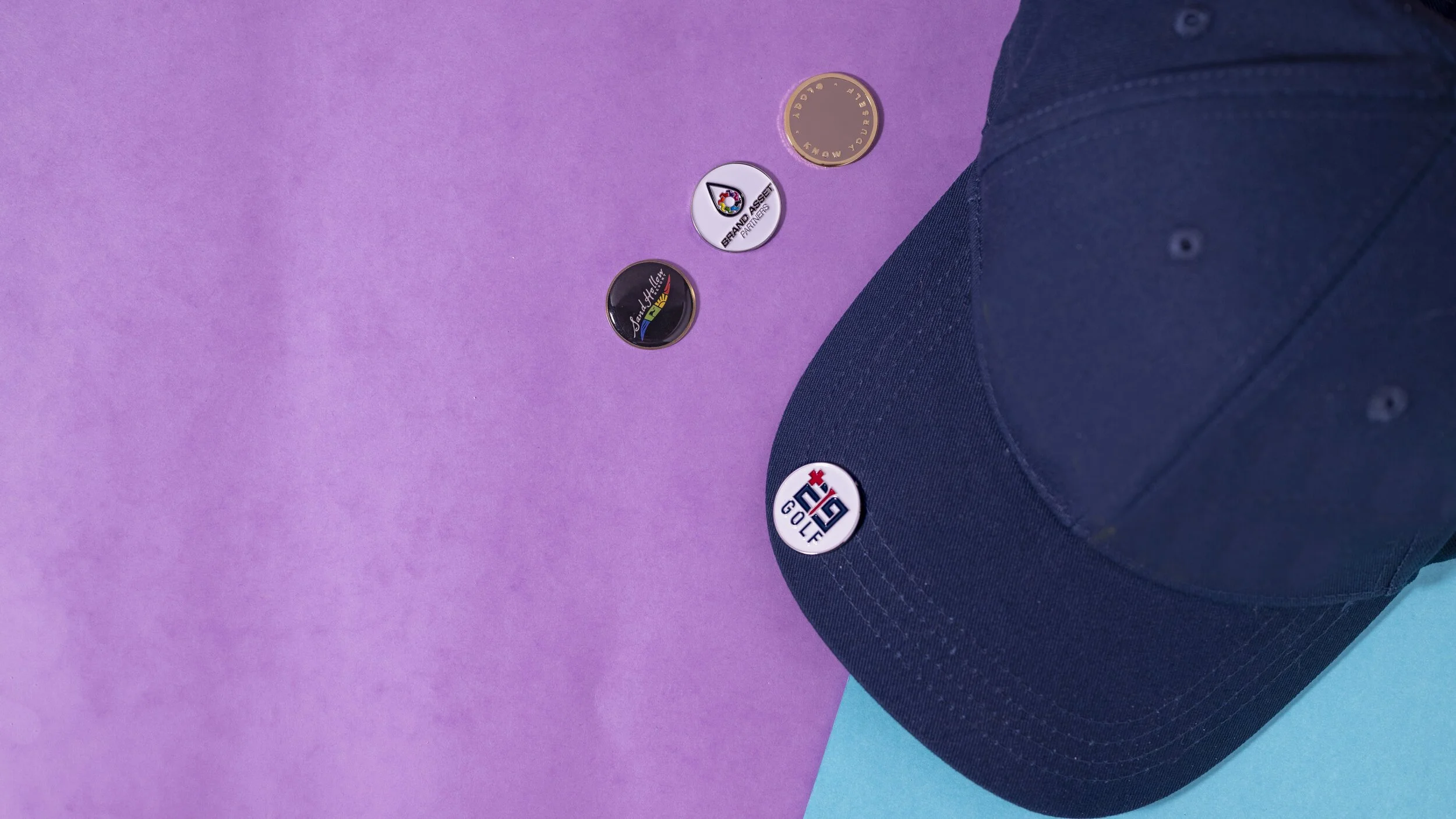 Custom golf ball markers clipped to the brim of a navy golf cap