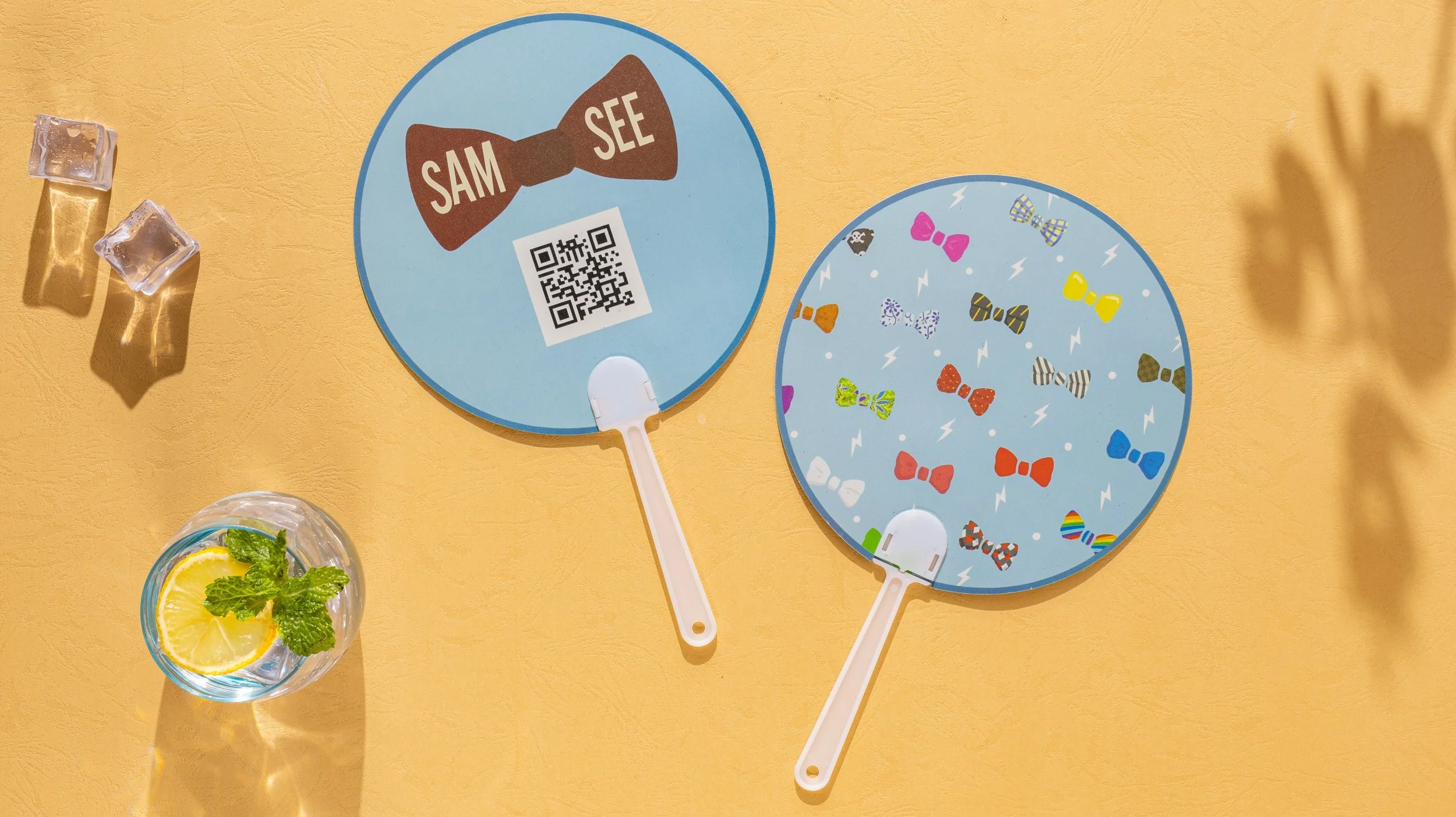 Two round hand fans for Sam See, one printed with the bow tie logo and QR code, one with an all over bow tie print