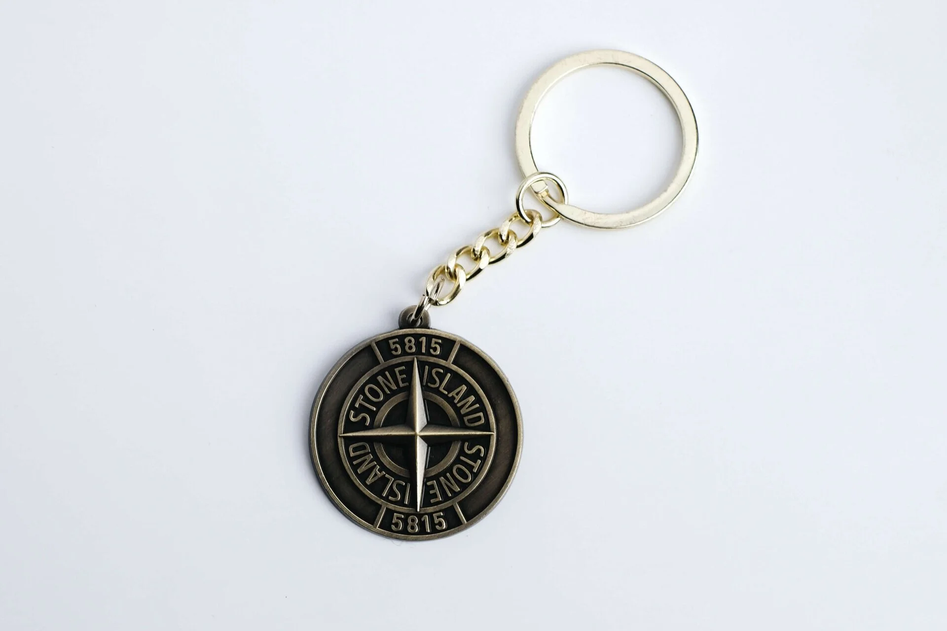 Die struck antique metal keychain with a Stone Island compass emblem in raised and recessed metal