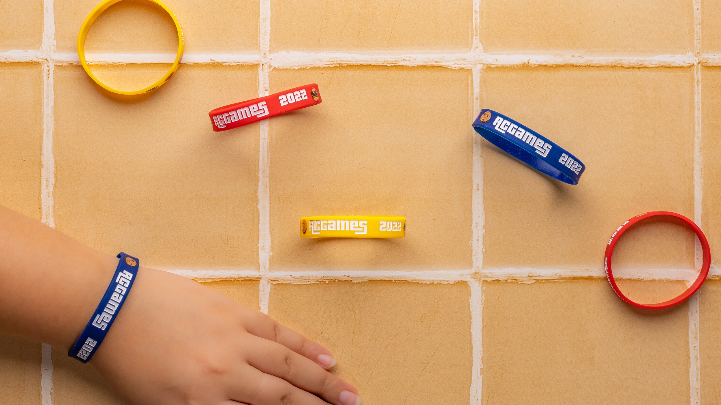 Coloured silicone wristbands printed with event branding on a tiled floor, one worn on a  wrist