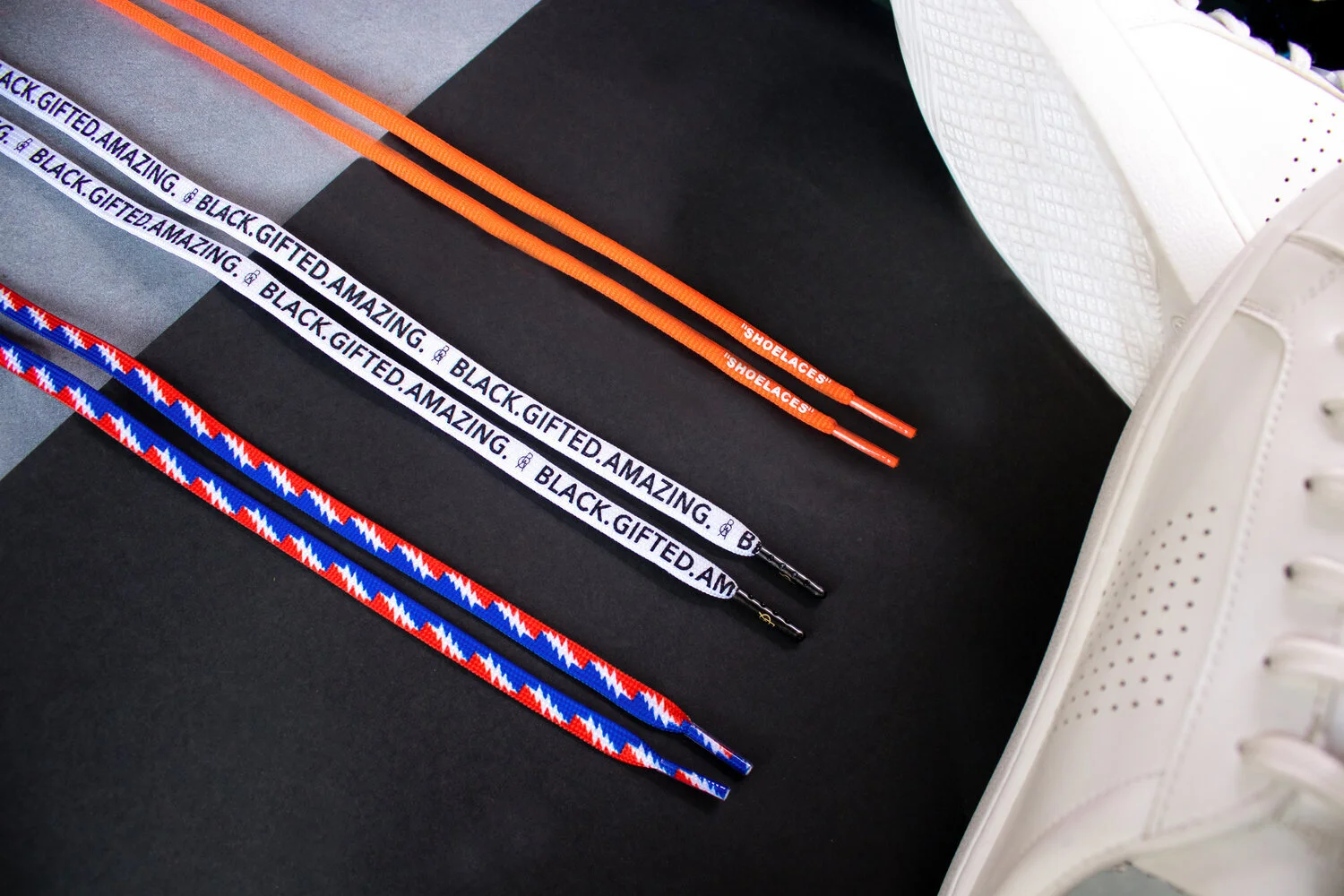 Printed custom shoelaces in patterned white and plain orange laid beside a white sneaker