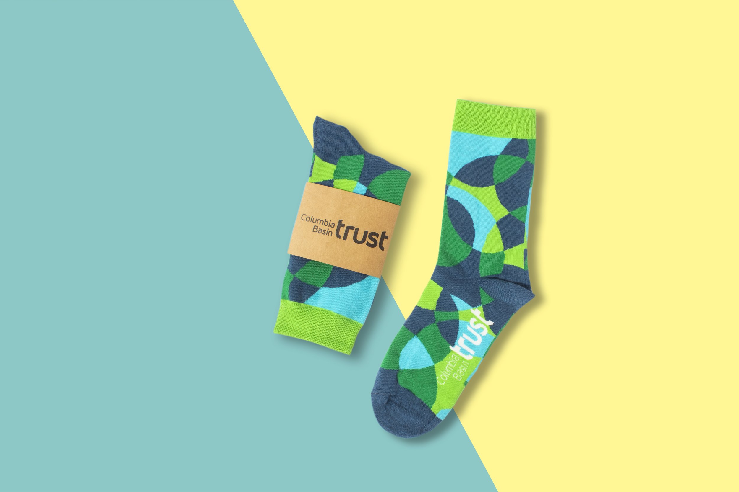 Custom socks in a green and blue geometric brand pattern, banded with kraft paper packaging