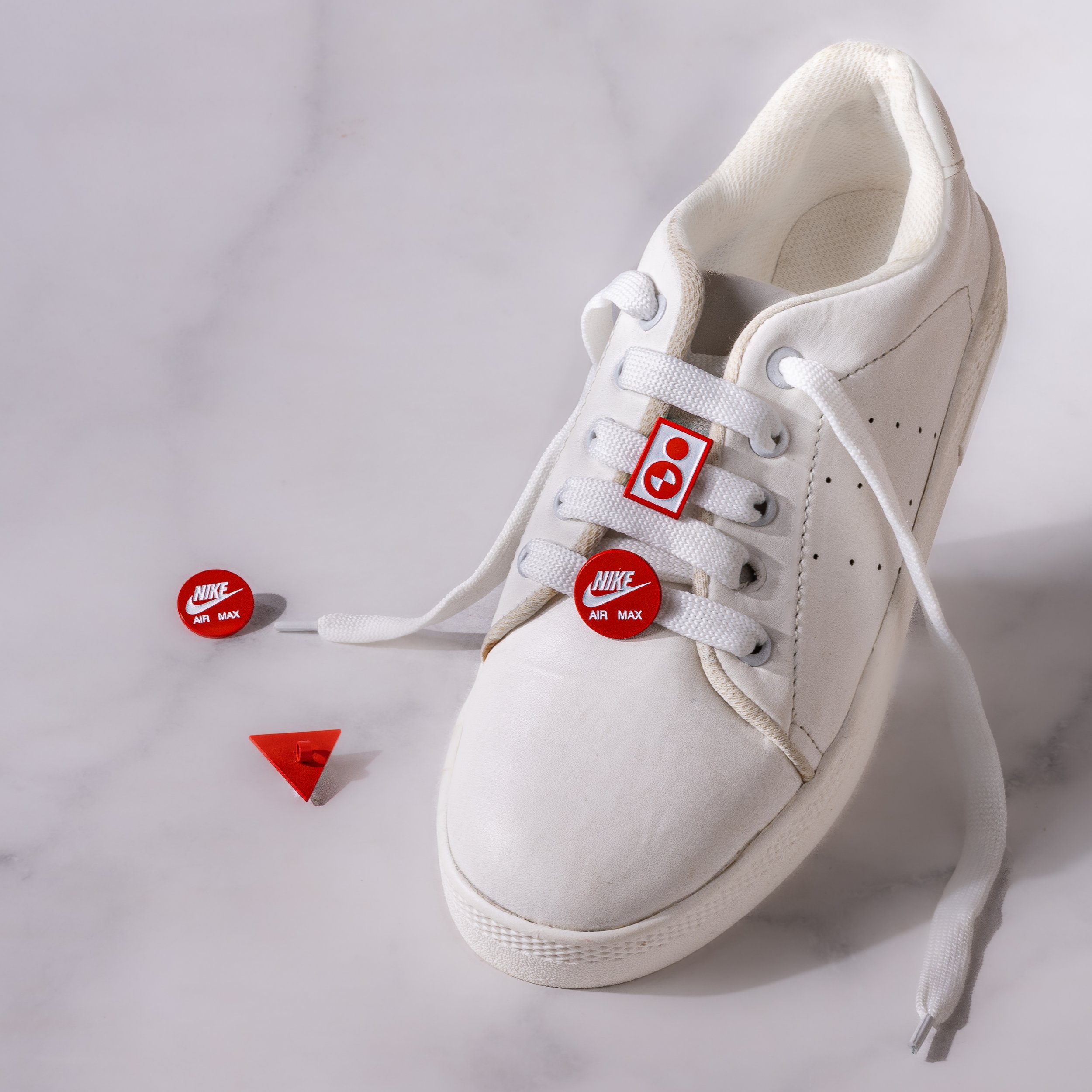 Nike Air Max round logo charm and red icon charm fitted to the laces of a white sneaker
