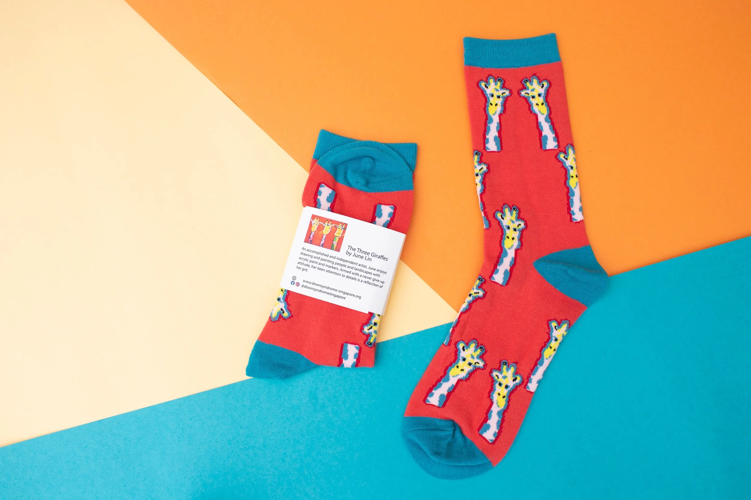 Red custom socks with a knitted giraffe artwork and a printed card telling the artist's story