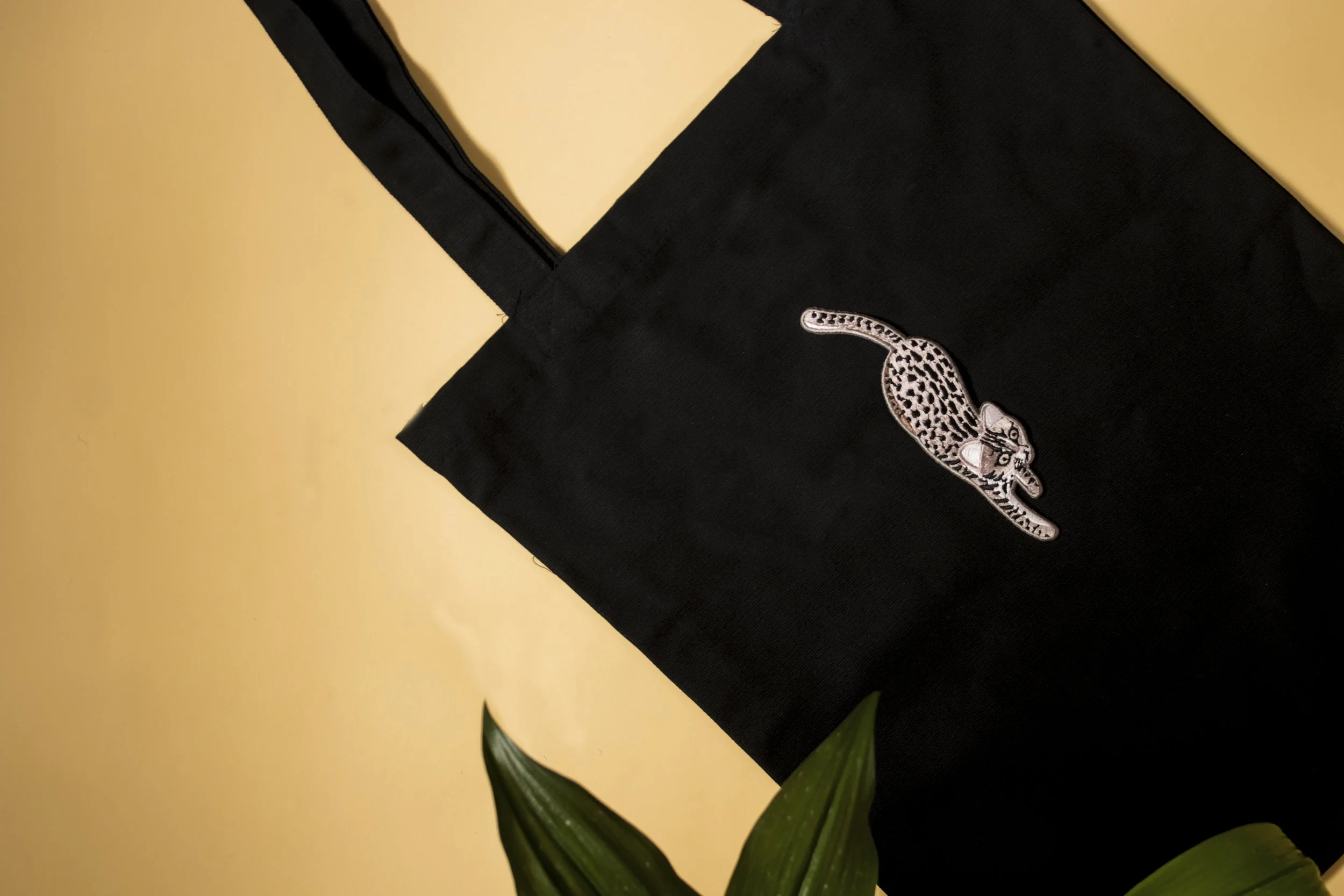 Detailed embroidered leopard patch stitched onto a black canvas tote bag