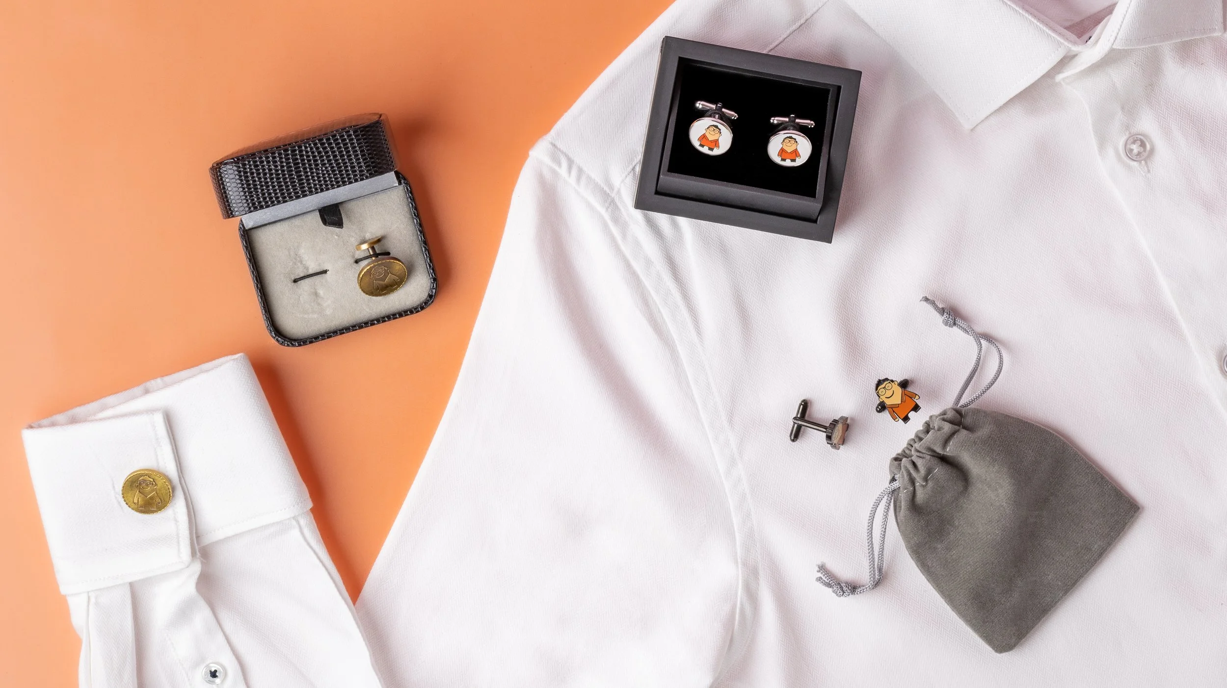 Custom cufflinks laid out on a white dress shirt with velvet boxes and a grey drawstring pouch