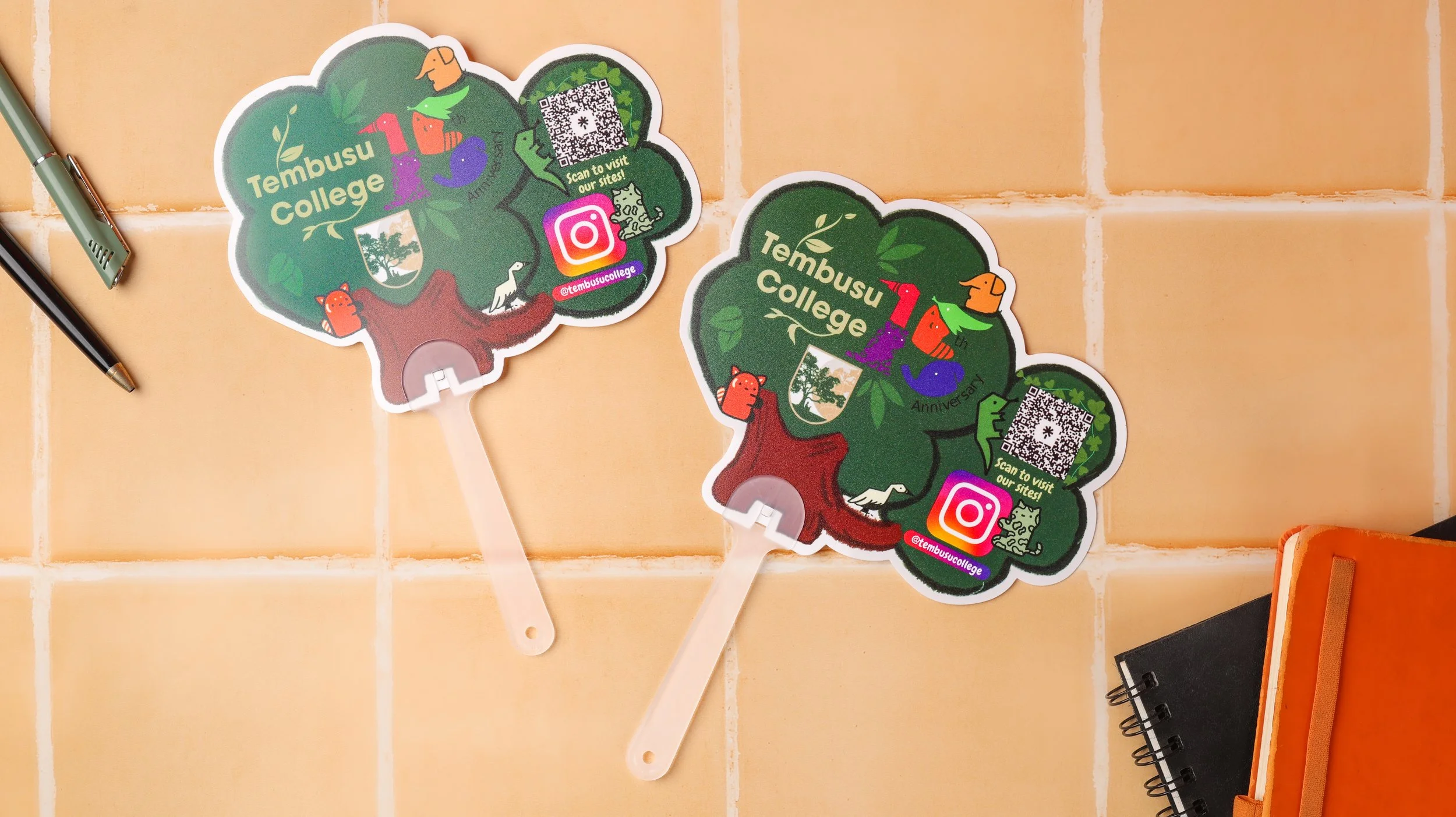 Two tree shaped die cut hand fans for Tembusu College's 10th anniversary, printed with characters and a QR code