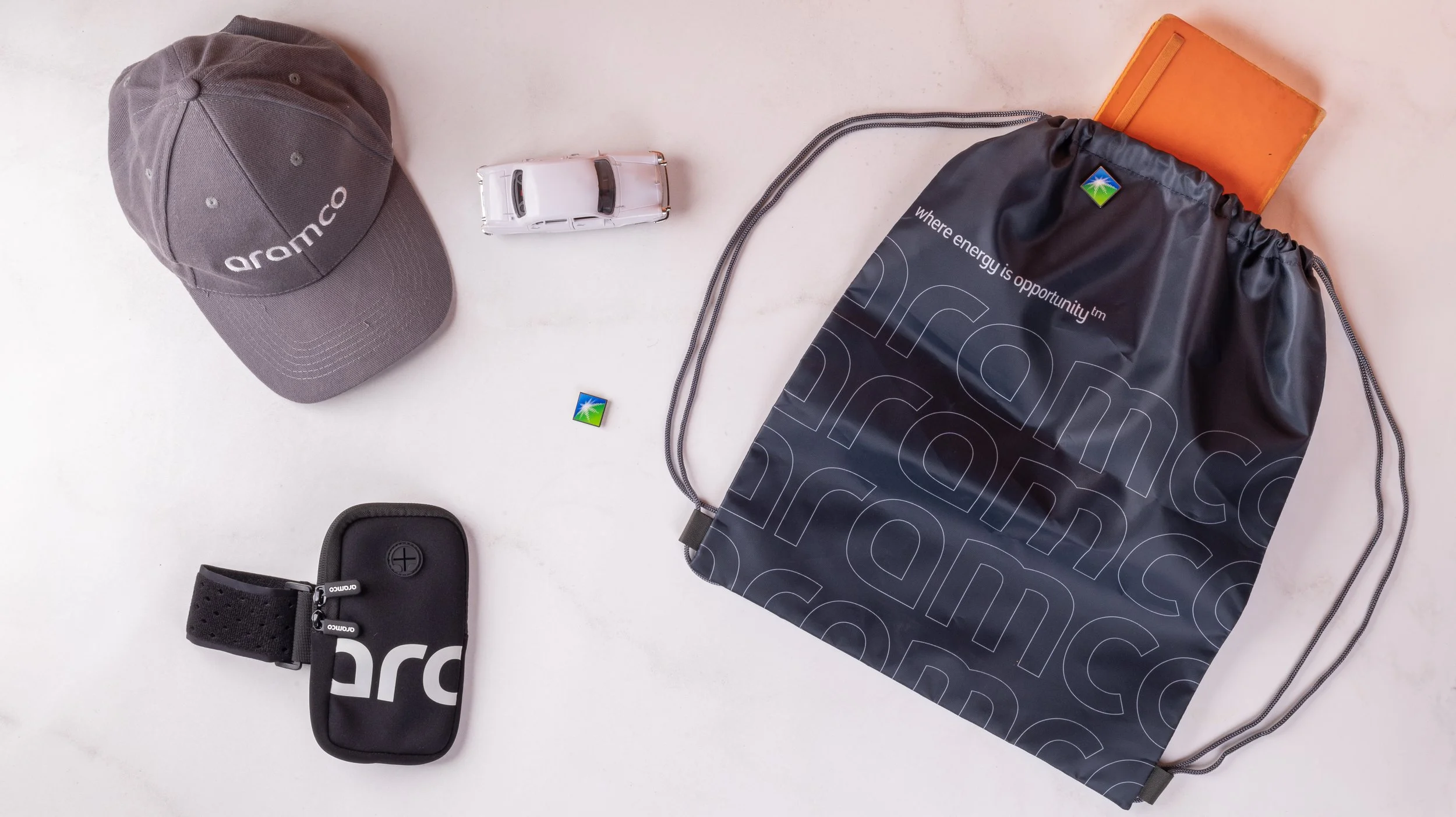Aramco branded merchandise kit with a cap, drawstring bag, enamel pin and phone armband