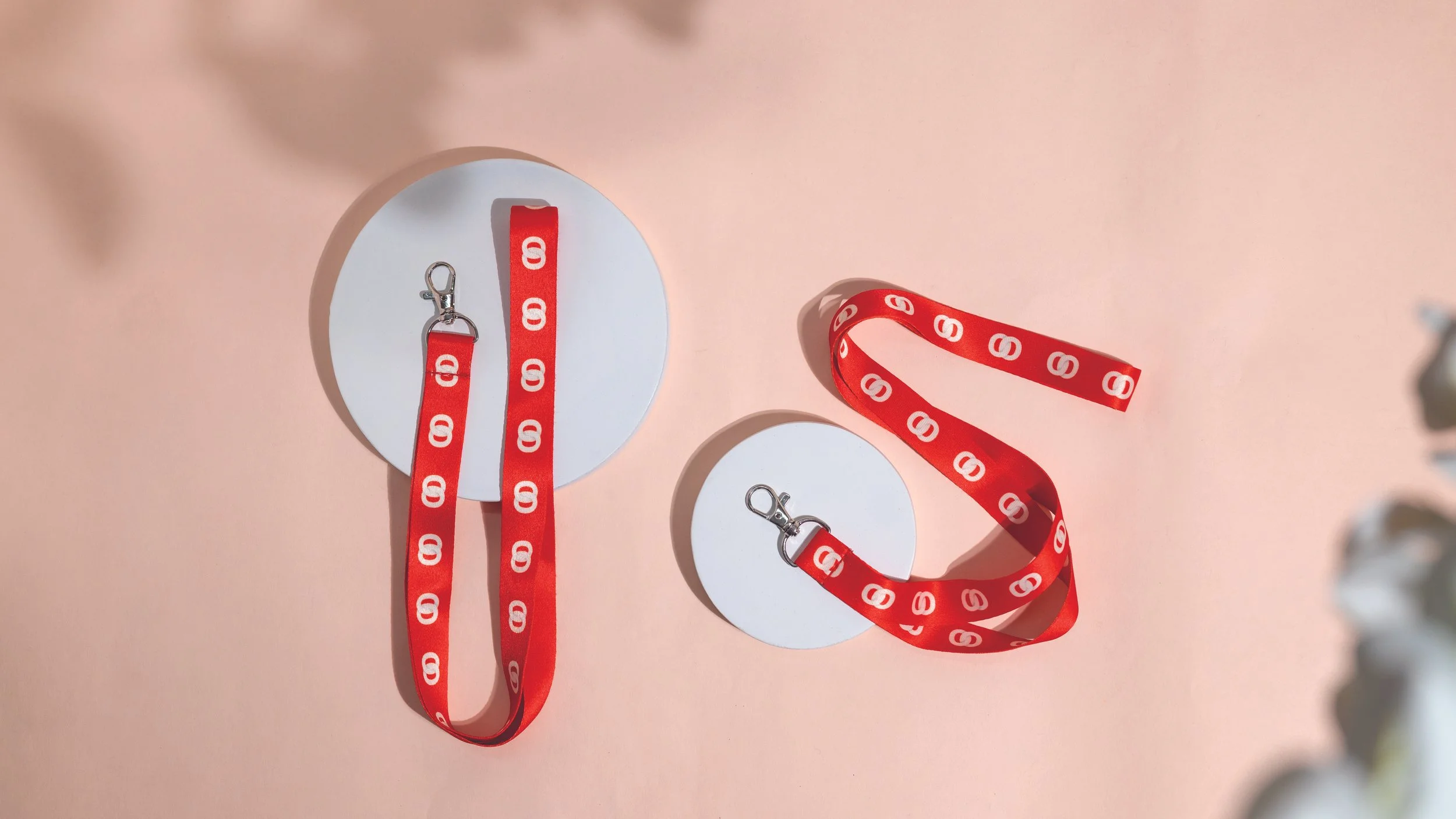 Two red lanyards printed with a 
repeating white logo, each 
clipped to a blank round white 
card