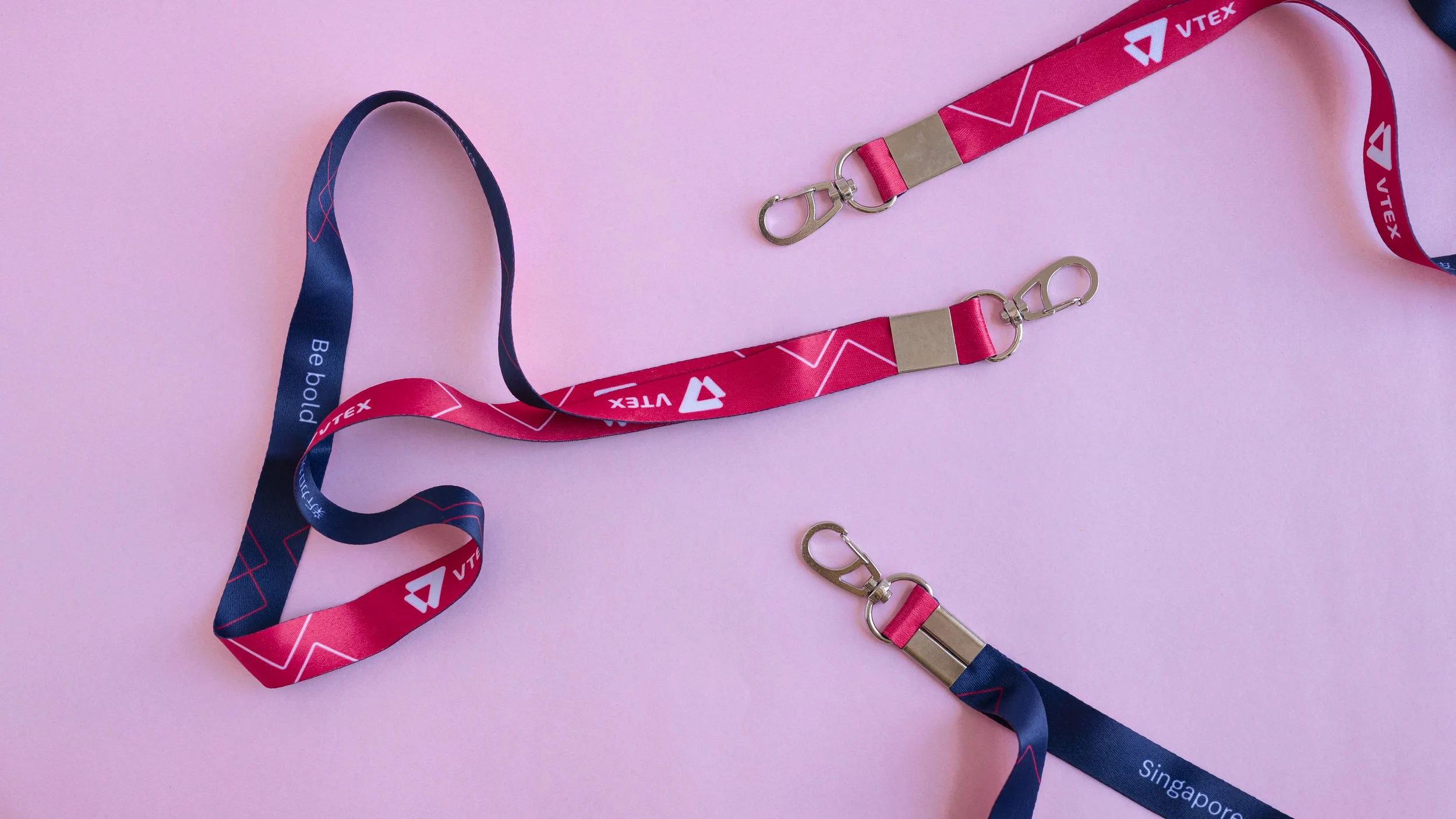 Red and navy VTEX lanyards 
with gold hardware, shown as a 
neck lanyard and two short 
wristlet straps