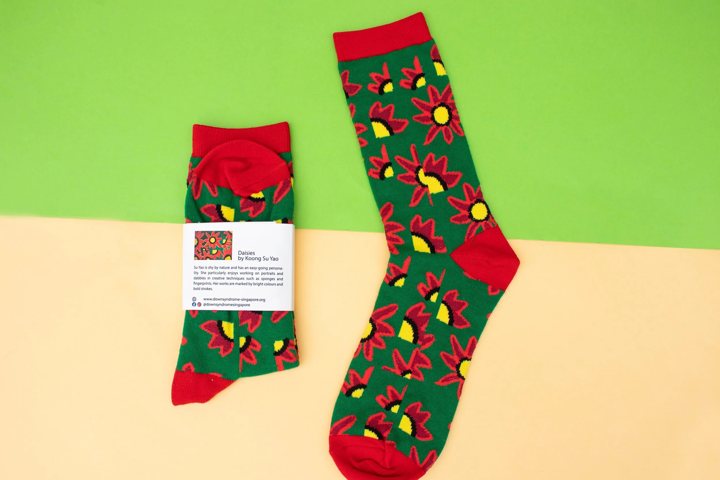 Green custom socks with a knitted red daisy artwork and a card telling the artist's story