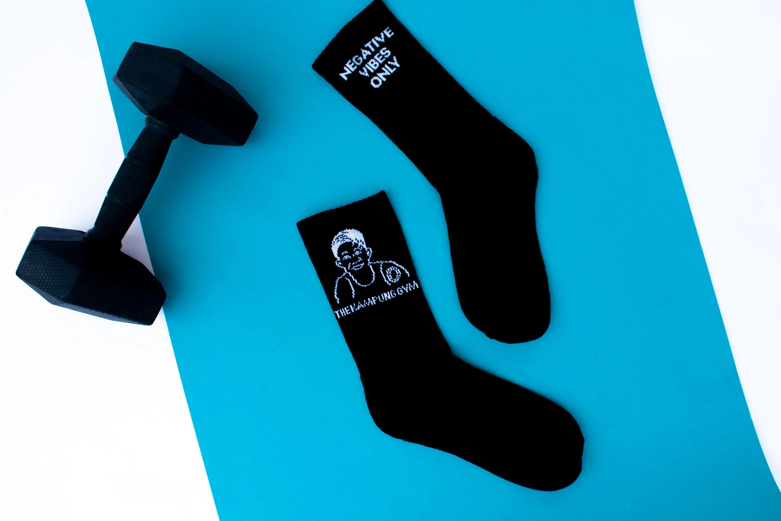 Black custom crew socks with a gym brand logo and slogan, photographed beside a dumbbell
