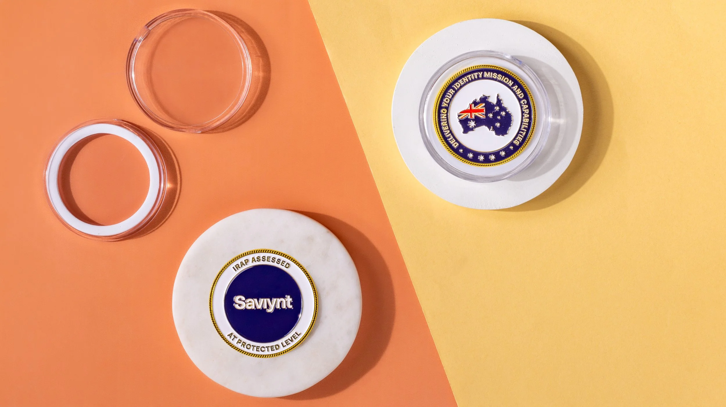 Two enamel coins in clear capsules — a Saviynt IRAP coin and an identity mission coin with an Australia map