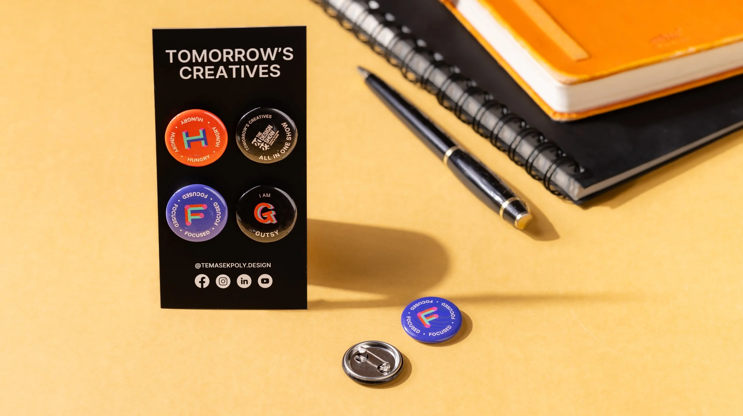 Four custom button badges 
on a Temasek Polytechnic 
Design Show backing card, 
with a loose Focused badge 
and pin back