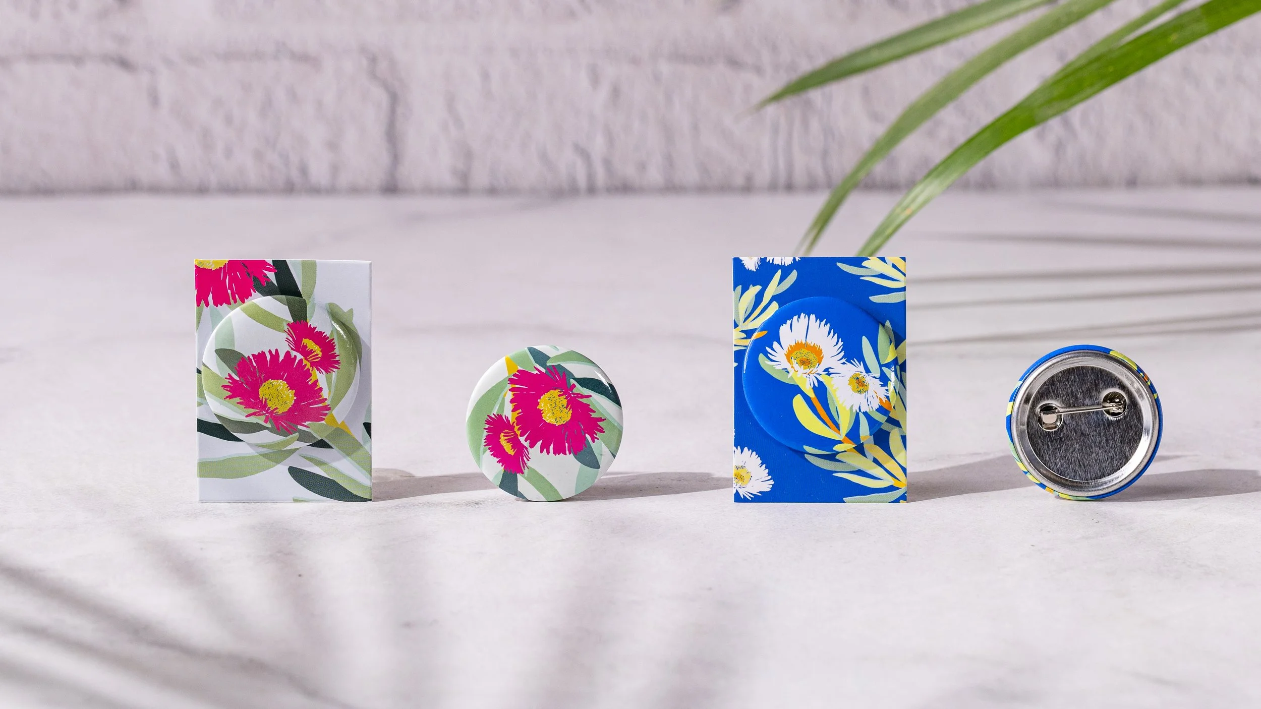 Two floral custom button 
badges on printed backing 
cards, with a loose badge 
and one turned to show the 
pin back