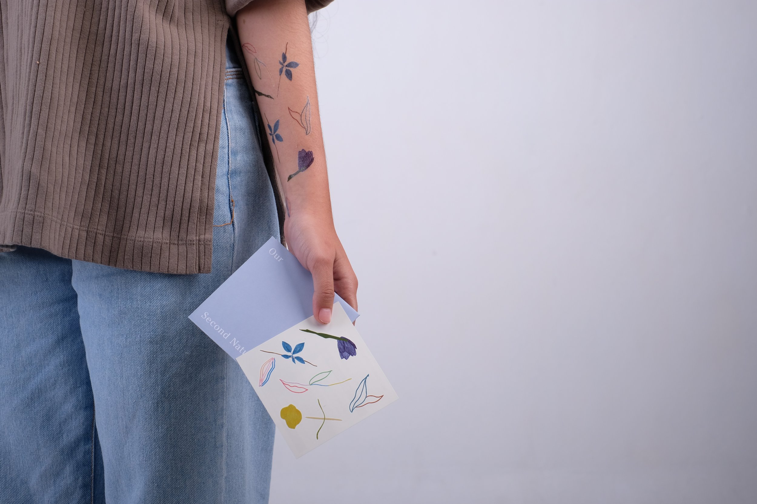 Floral line art temporary tattoos on a forearm beside the printed tattoo sheet and its envelope