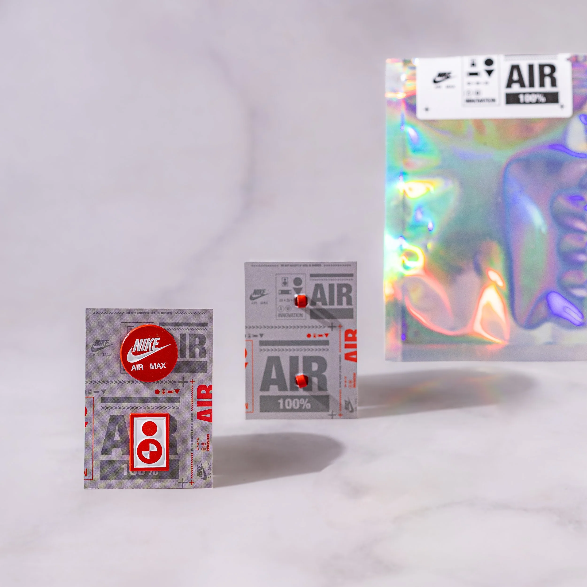 Nike Air Max charms on printed backing cards, a round logo charm and a red icon plaque, beside a holographic pouch