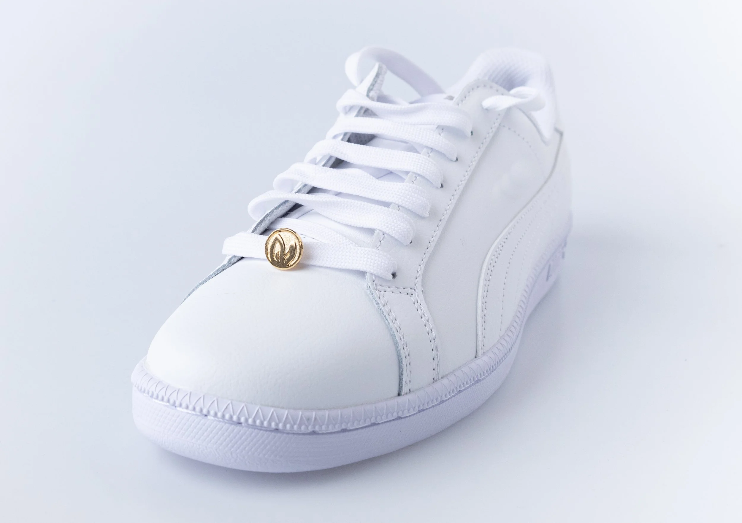 Small gold shoe charm with an engraved Chinese New Year Rabbit of the Year emblem clipped to the laces of a white sneaker