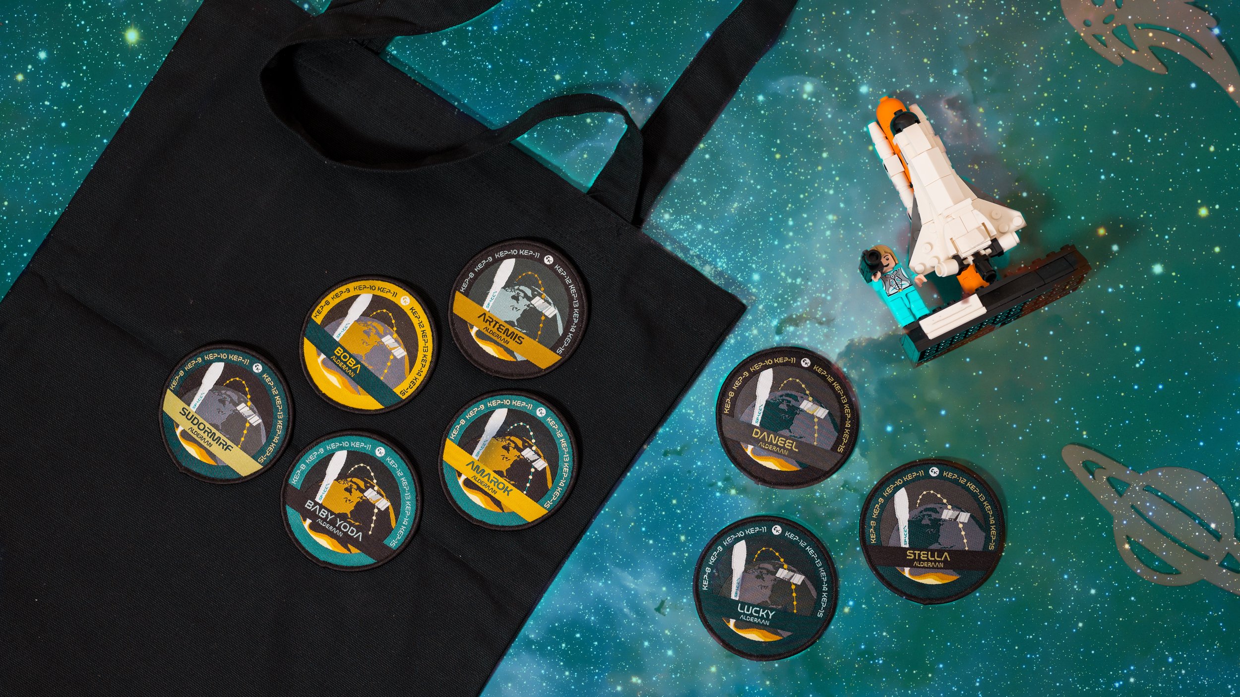 Eight woven mission patches with individual crew names on a black tote bag beside a Lego space shuttle