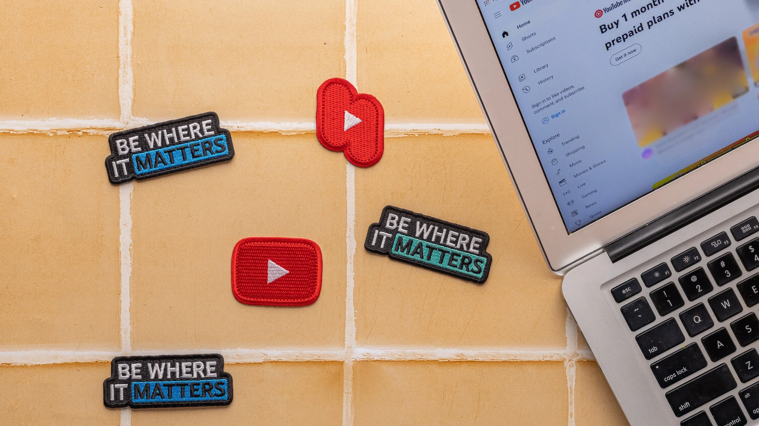 YouTube play button and Shorts patches with Be Where It Matters slogan patches beside a laptop