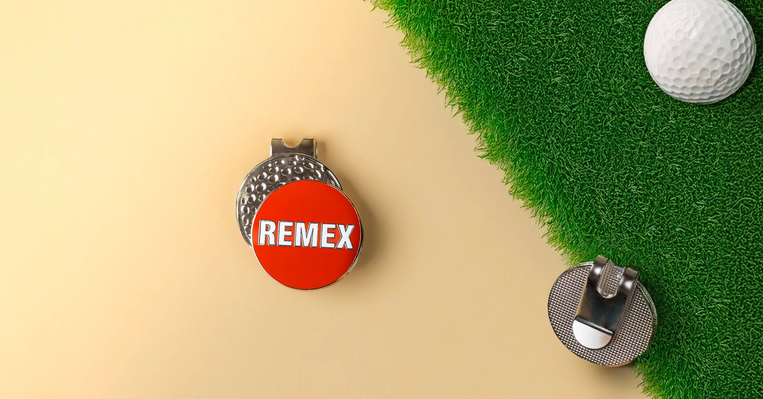 Red and white Remex logo golf ball marker on a golf-ball textured hat clip, with the clip reverse